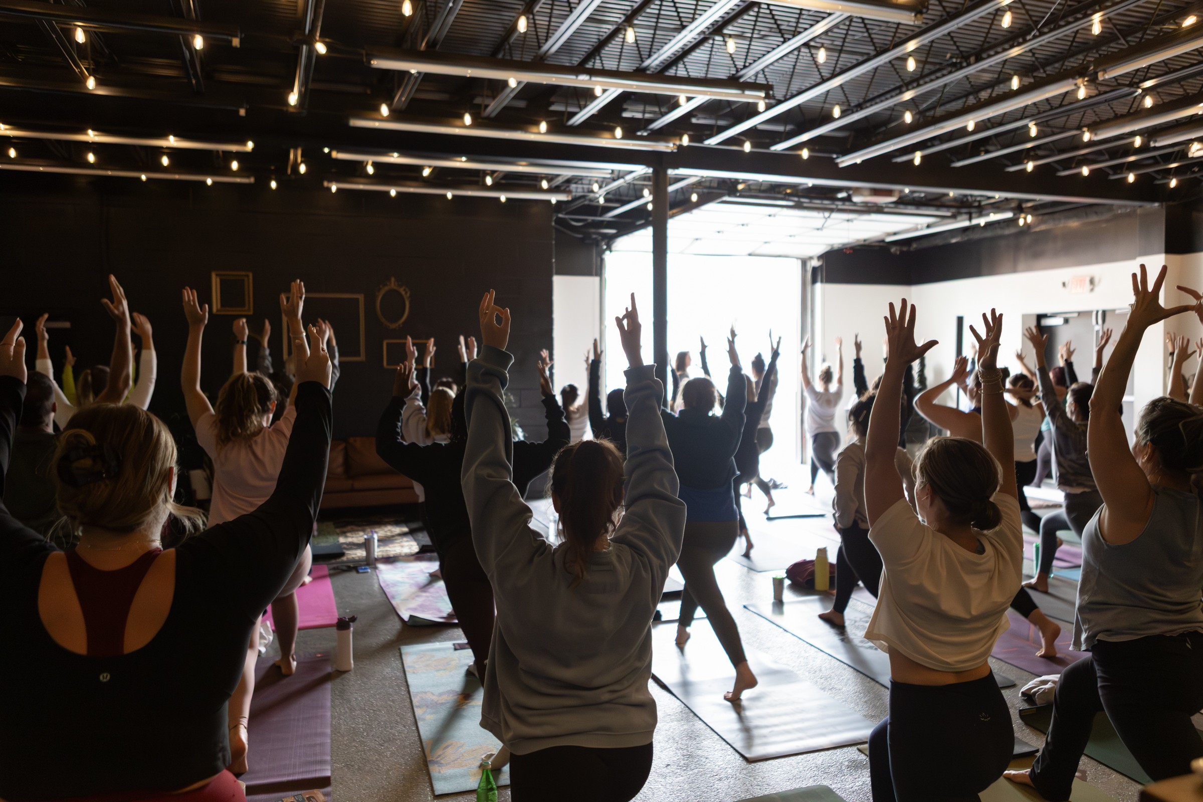 People participating in a group yoga or exercise class with raised hands in a spacious, well-lit studio.
