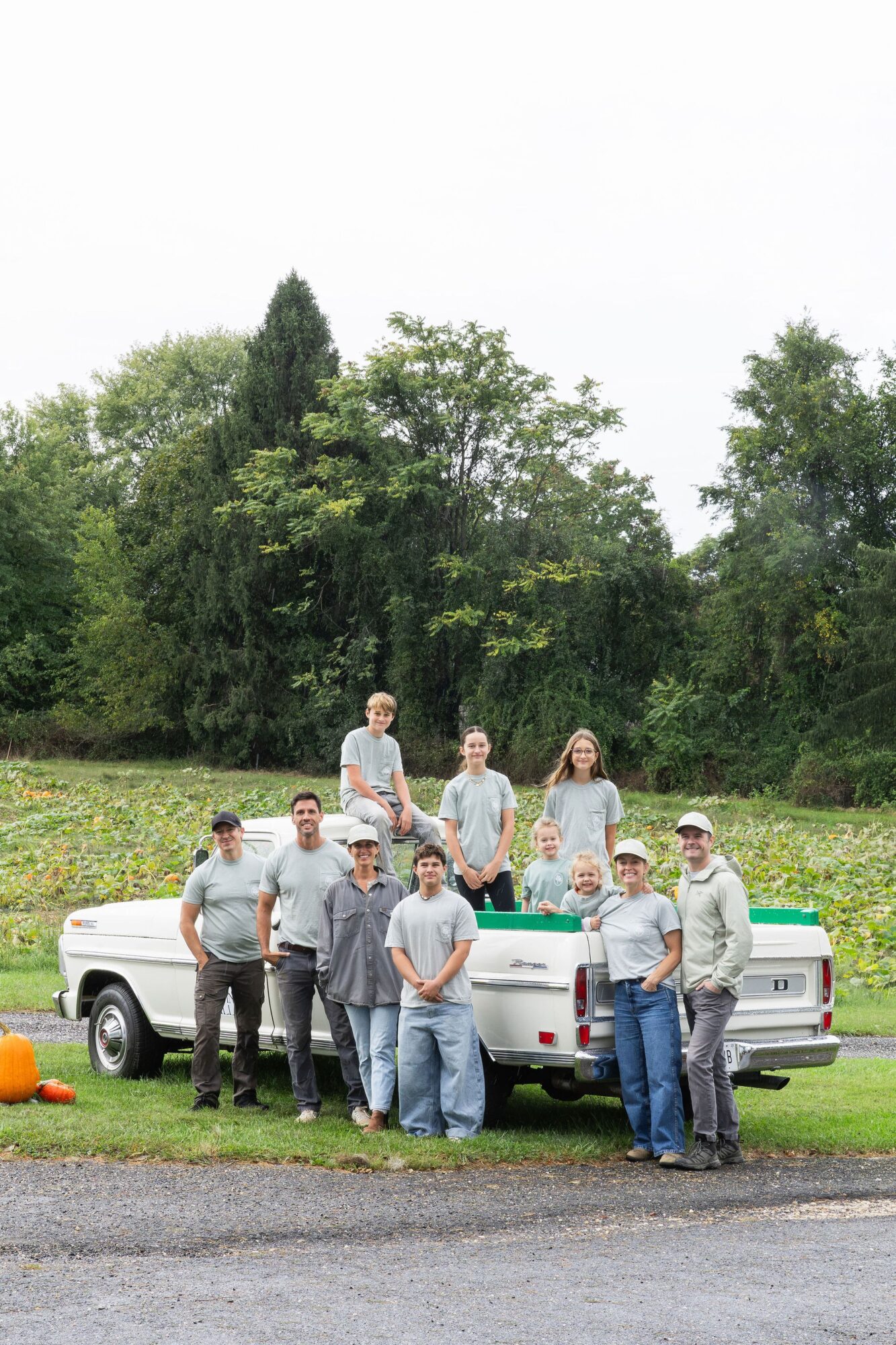 Group of nine people outdoors near a white pickup truck, with trees and grass in the background.
