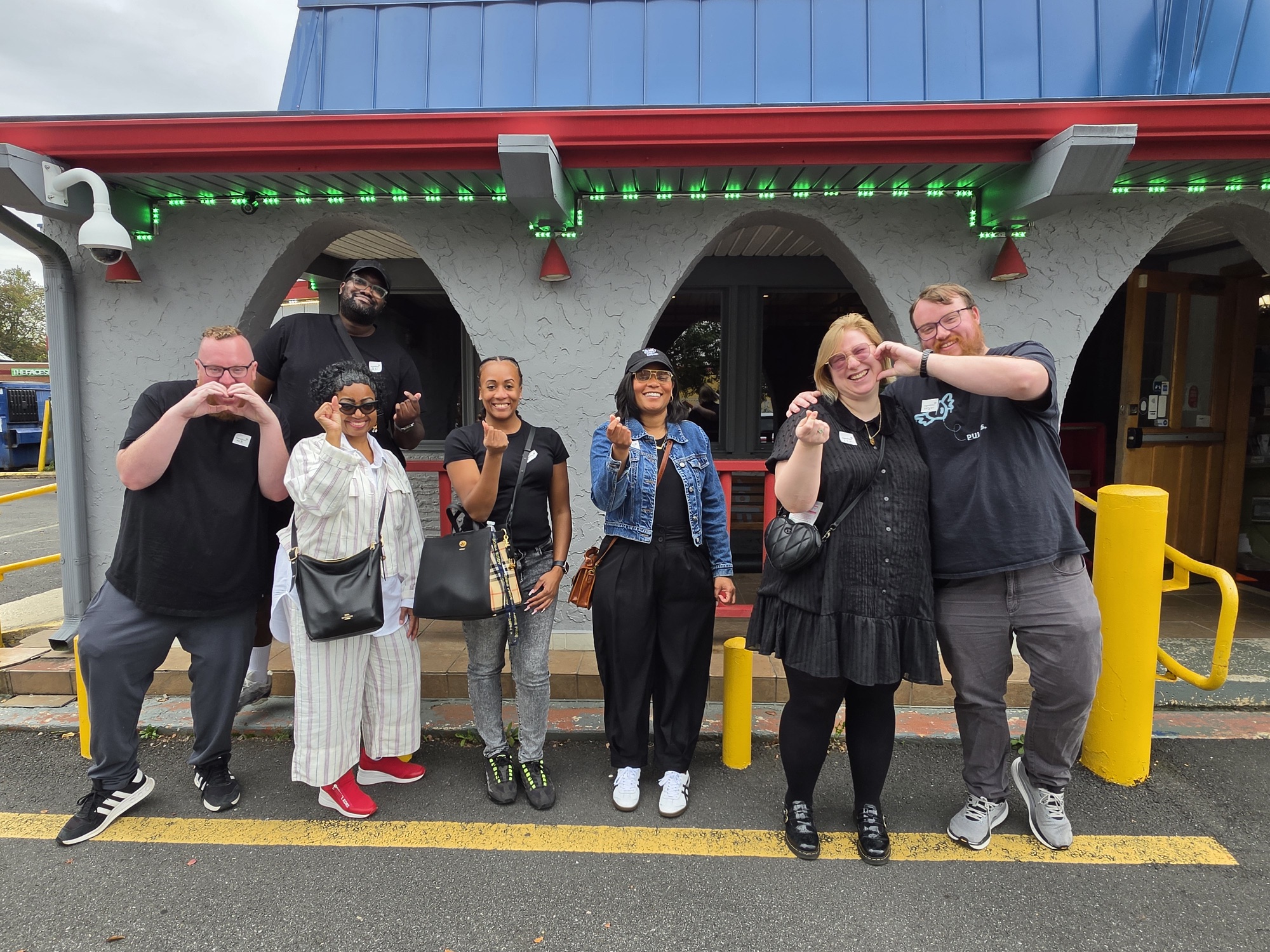Group of seven people standing outside a building with arches, some taking photos, smiling, and posing.