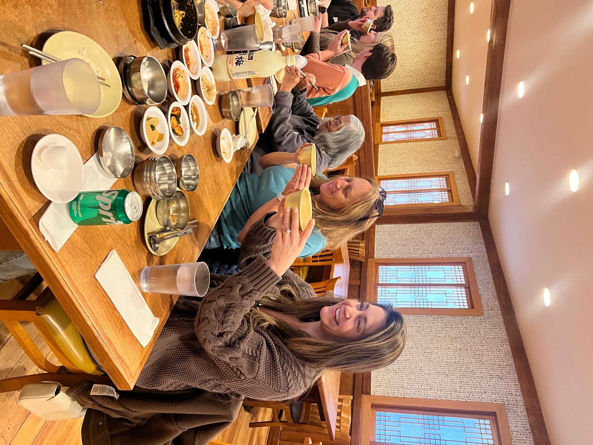Group of people gathered around a table with food and drinks in a warmly lit room, engaging in conversation and serving food.
