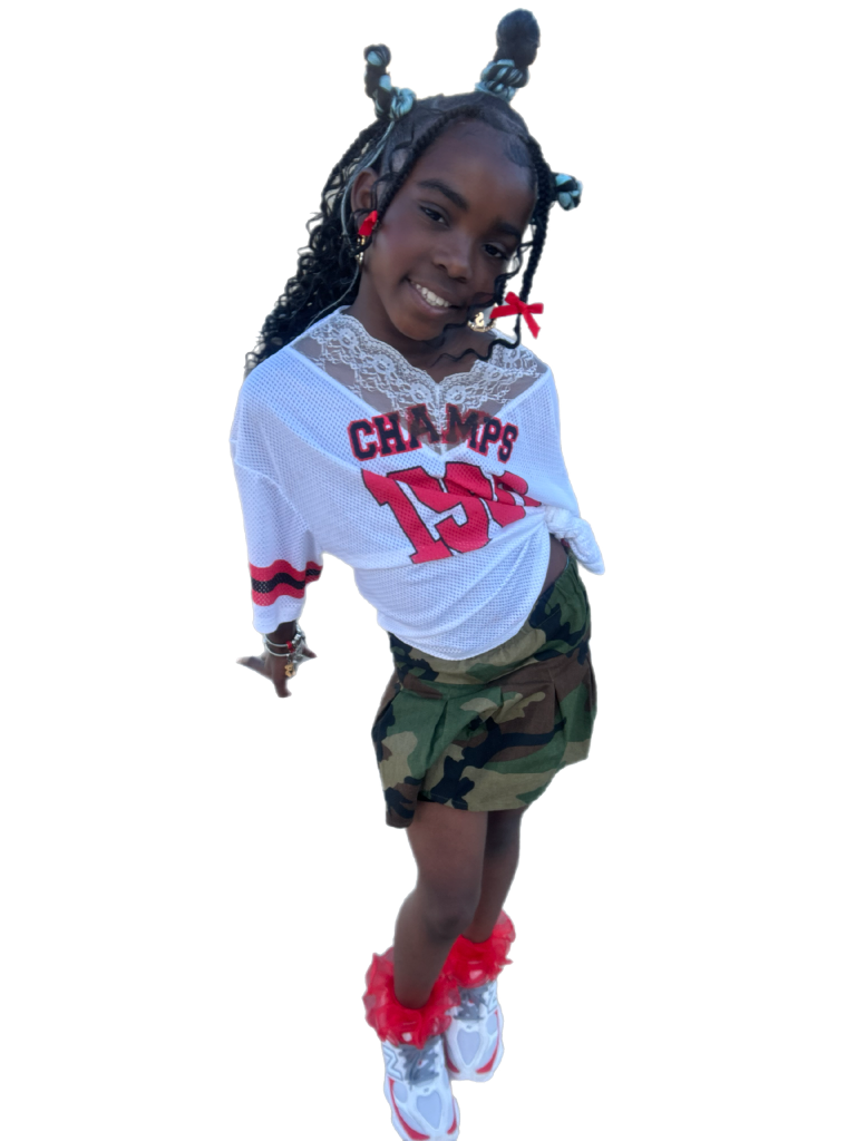 A person wearing a white sports shirt, camouflage shorts, and bright red-and-white shoes, with decorative hair accessories.