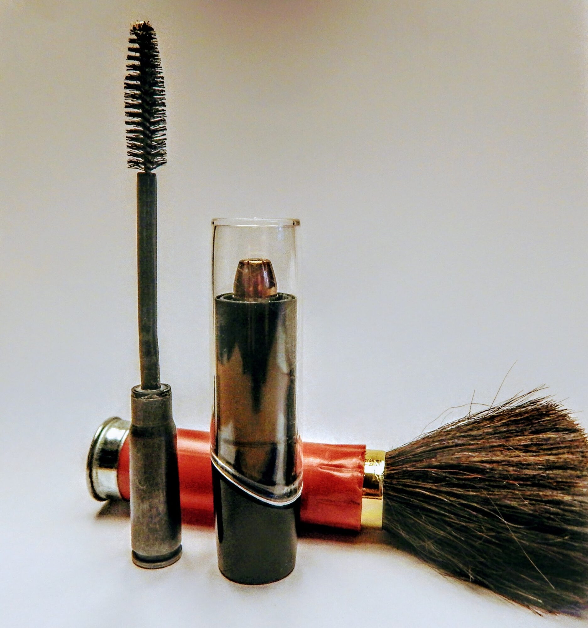 Makeup brush, mascara, and lipstick on a plain background, arranged vertically and horizontally.