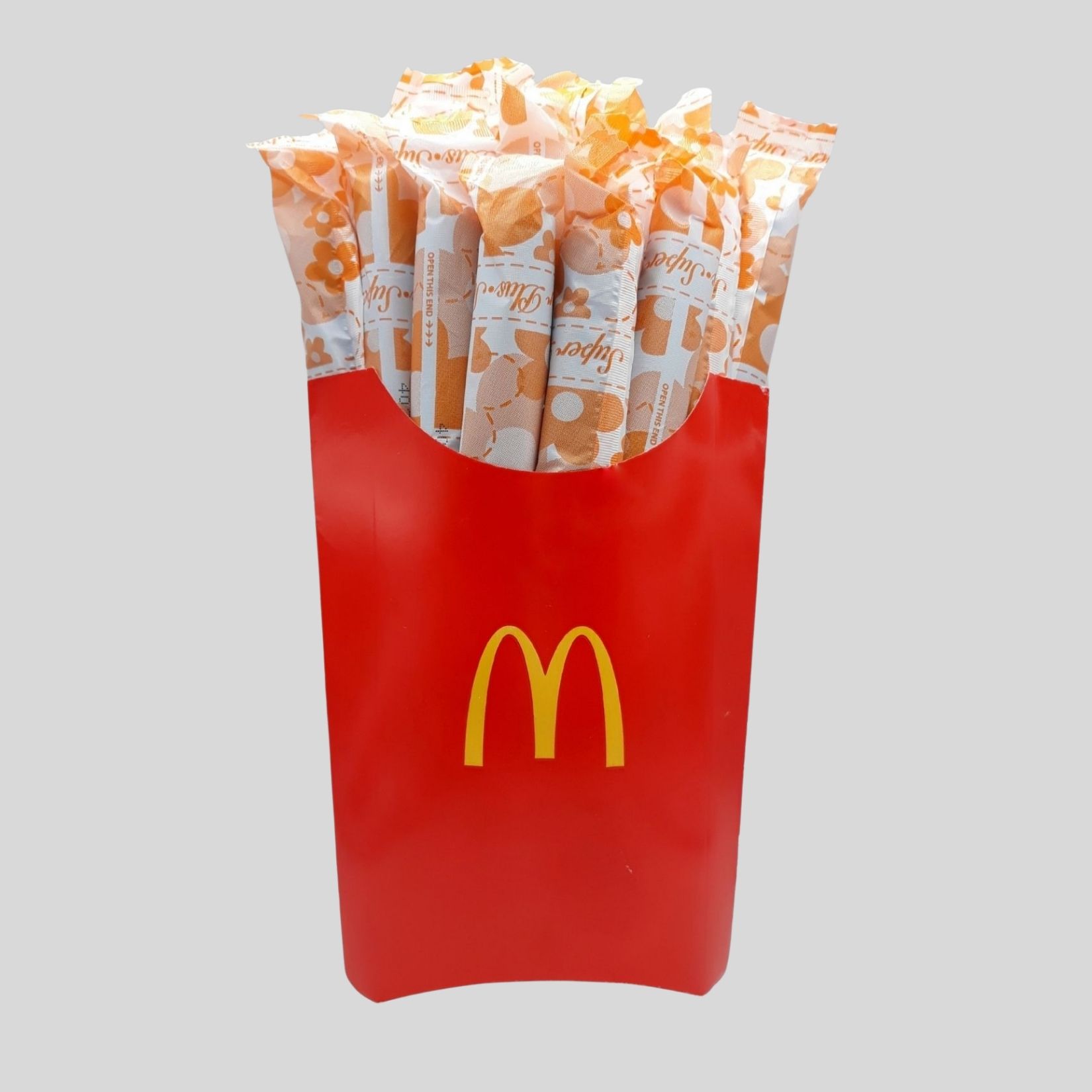A red McDonald's fries container filled with wrapped fries, with a yellow McDonald's logo, on a gray background.