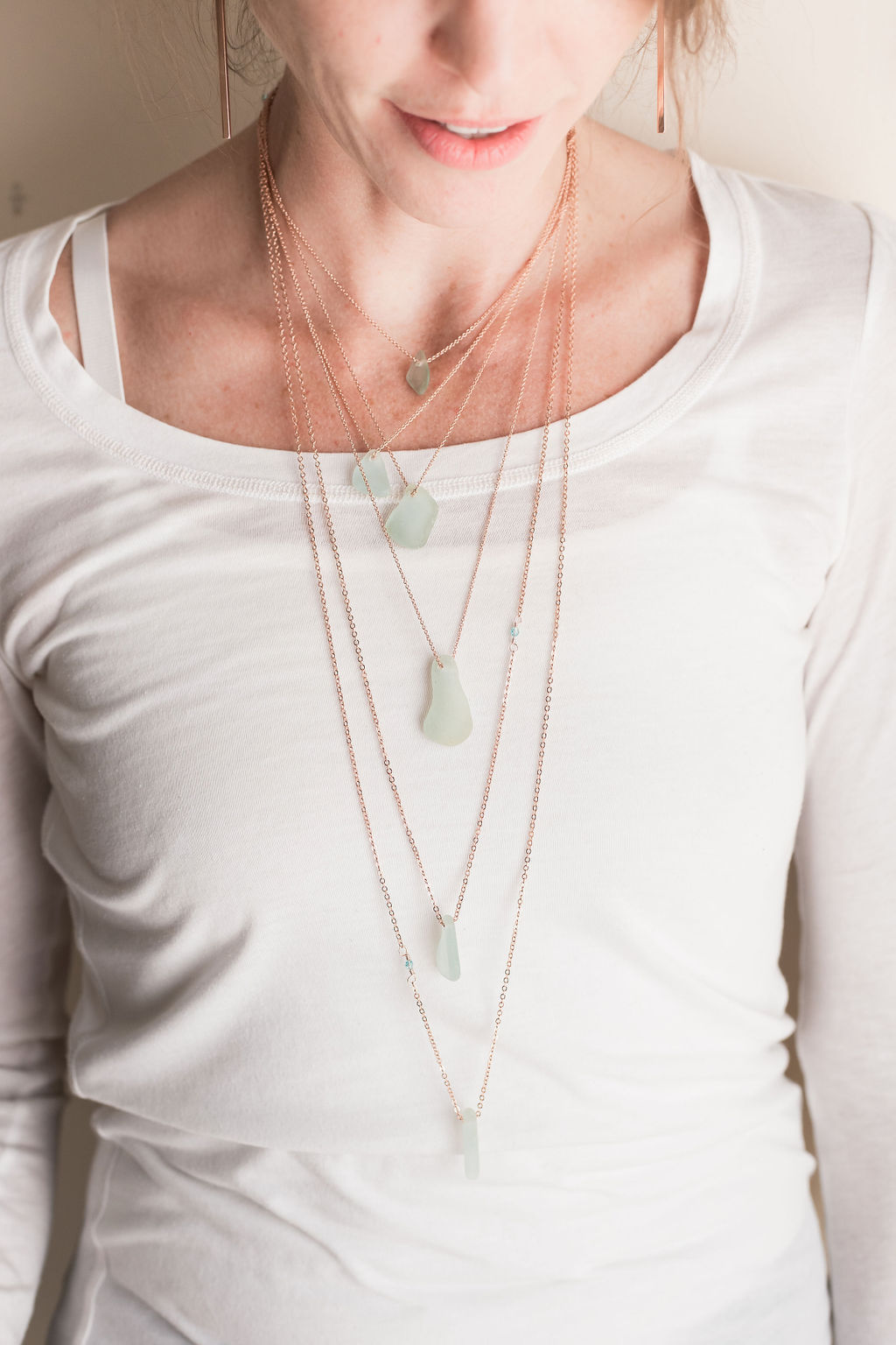 Close-up of a woman wearing layered necklaces over a white top, showing her neck and upper chest area.