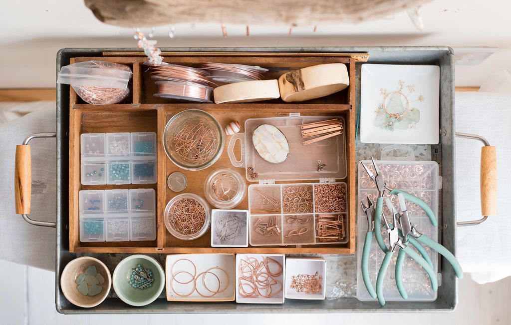 Jewelry-making supplies including beads, rings, pliers, and storage containers on a tray.