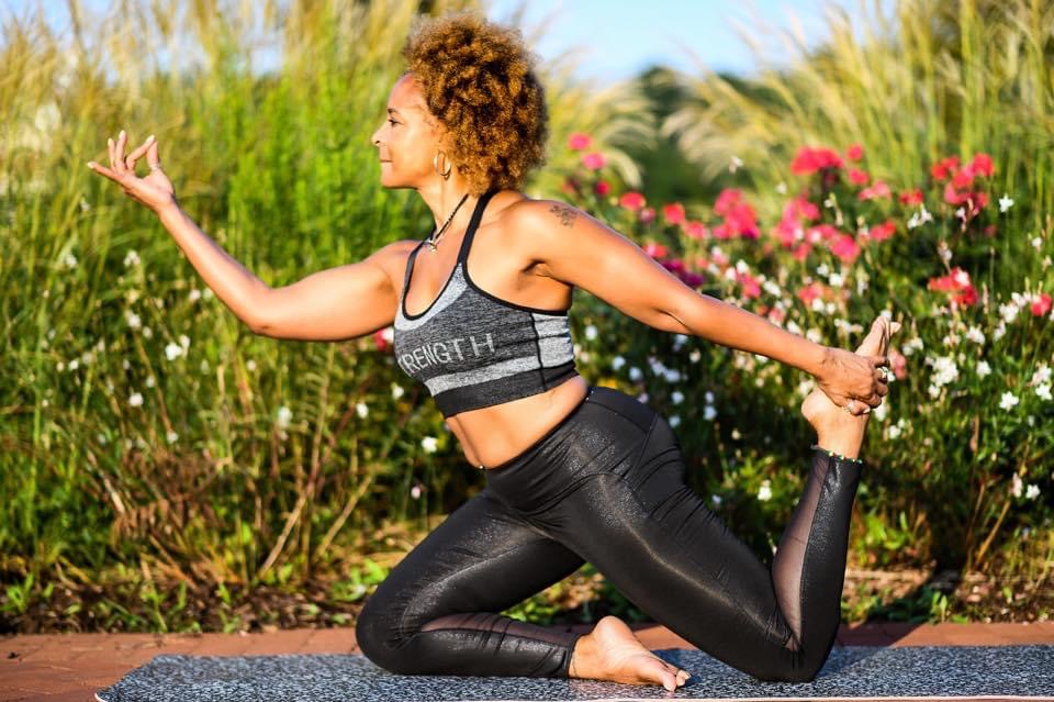 Woman practicing yoga outdoors on a mat with flowers and greenery in the background.