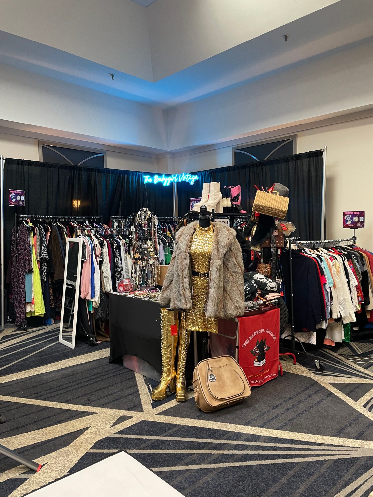 Clothing racks and folded garments fill a retail display beside a patterned carpet.