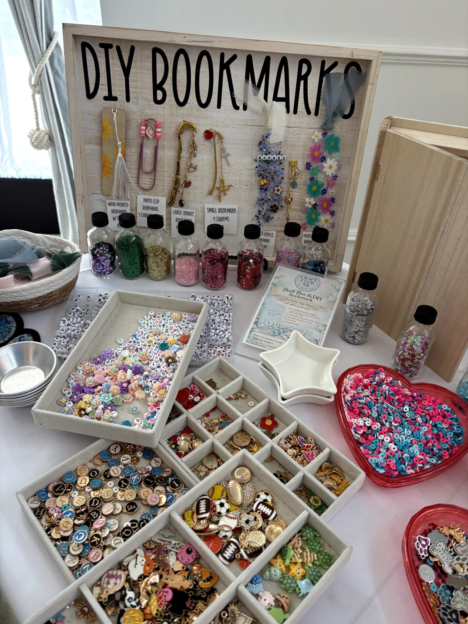 A display of handmade bookmarks and trays of colorful beads, charms, and craft supplies on a table.