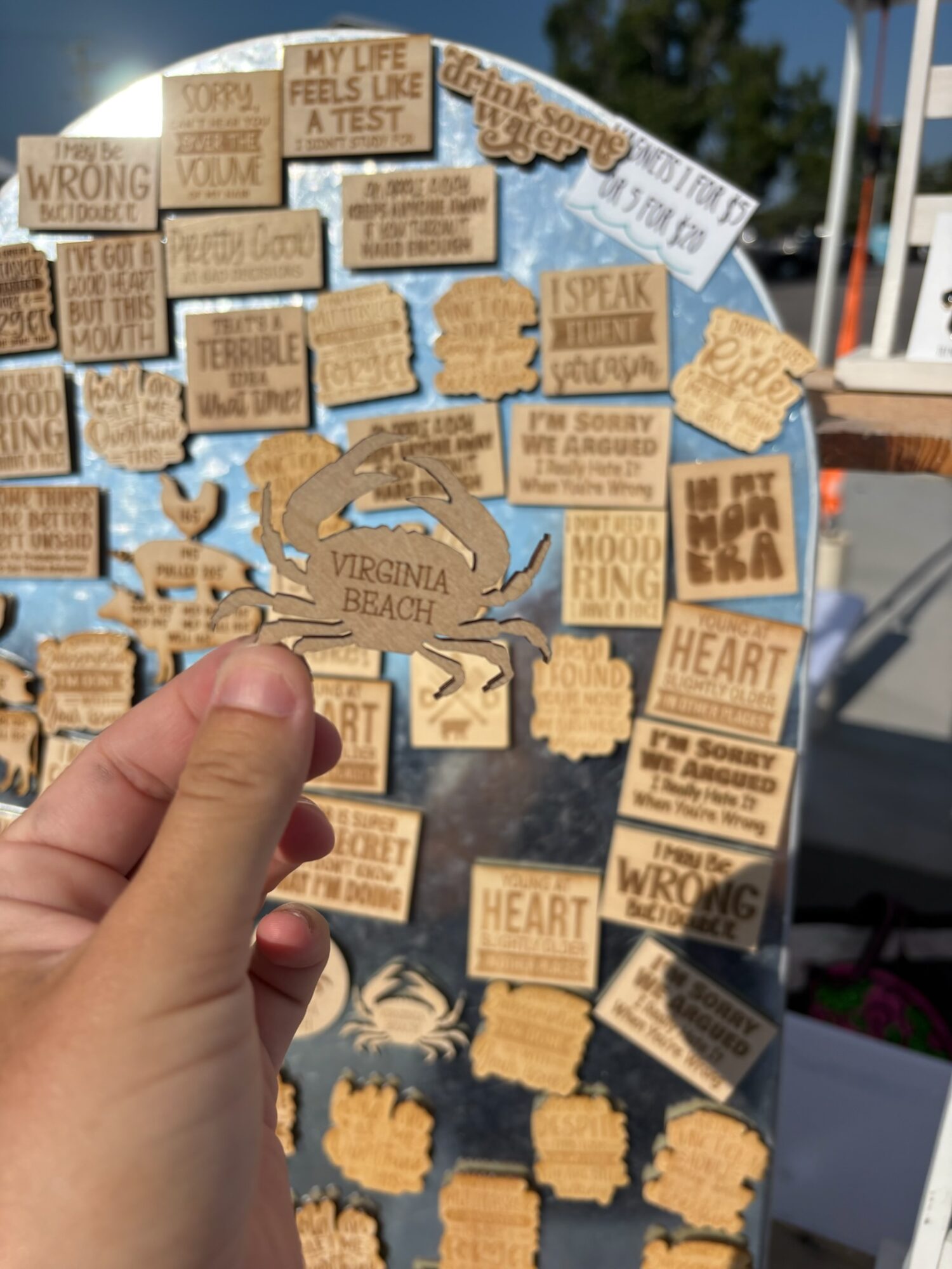 A hand holds a map covered with small quote plaques, with a marina and boats in the background.