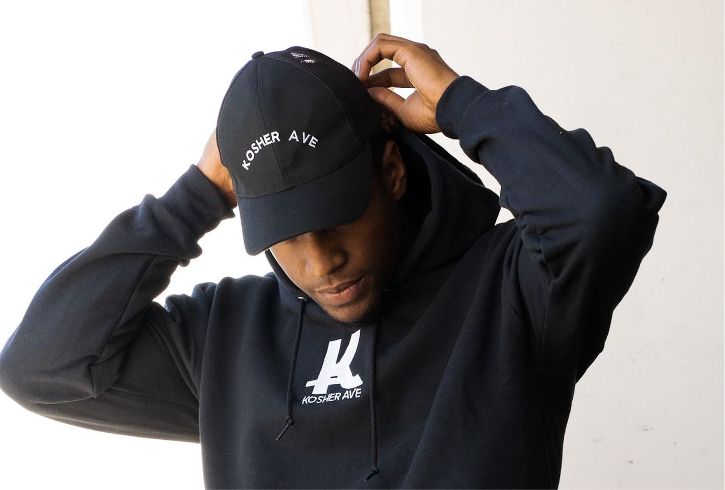 Person in a dark hoodie and cap, adjusting the cap with both hands.