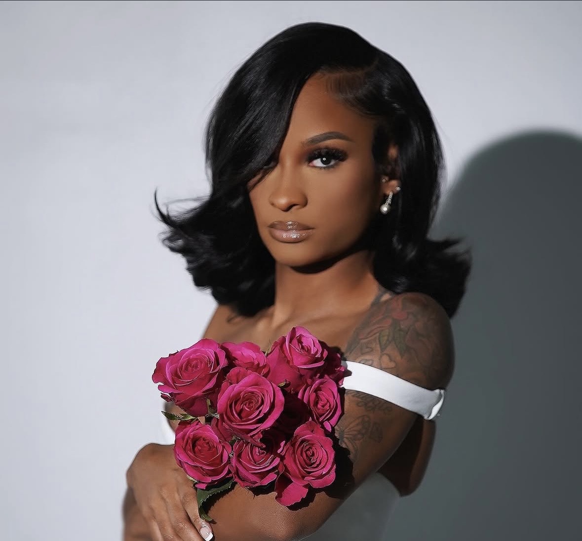 Person with dark hair holding a bouquet of pink roses, wearing a white off-shoulder top.