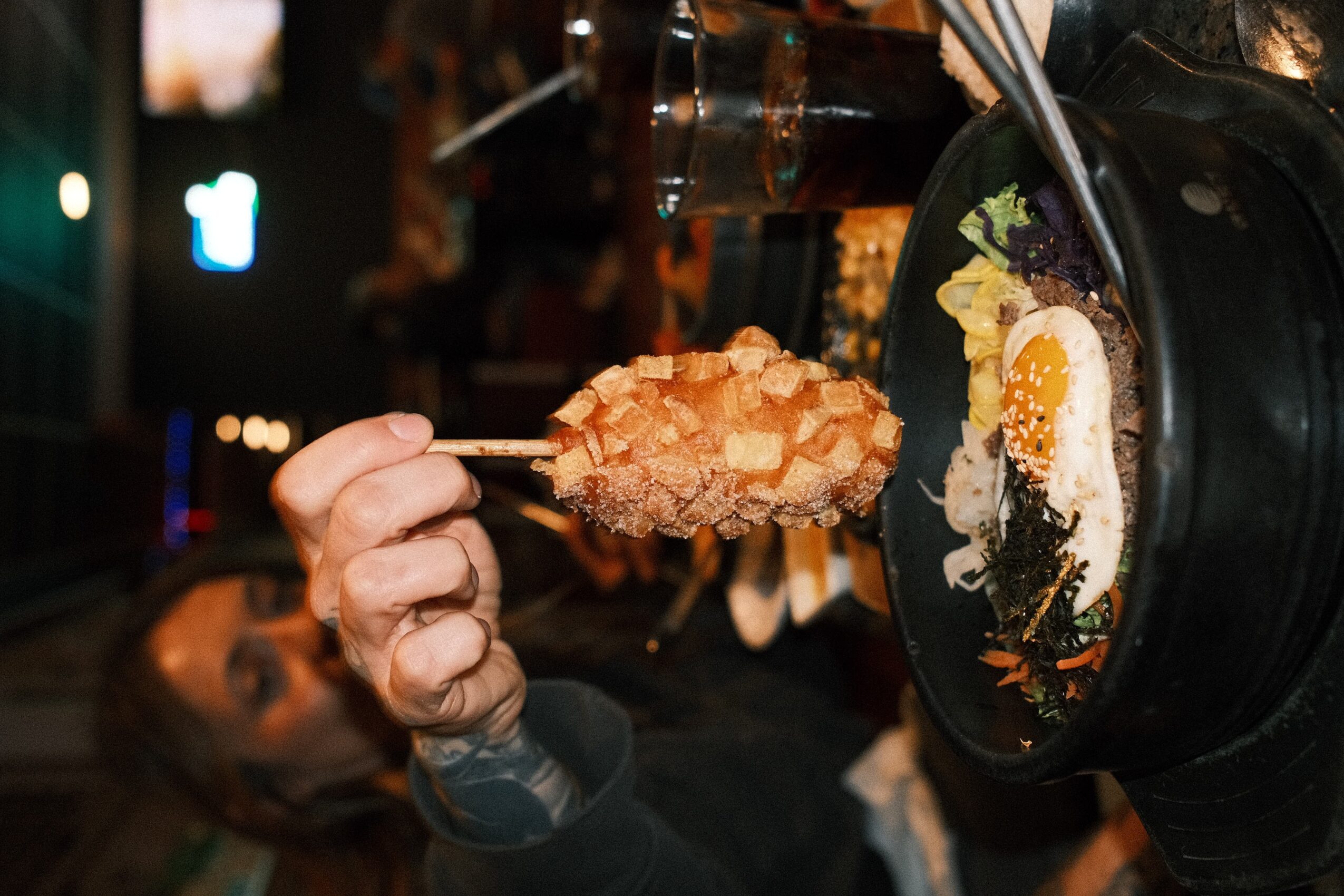 A person holds a spoonful of food beside a pan containing an egg and herbs.