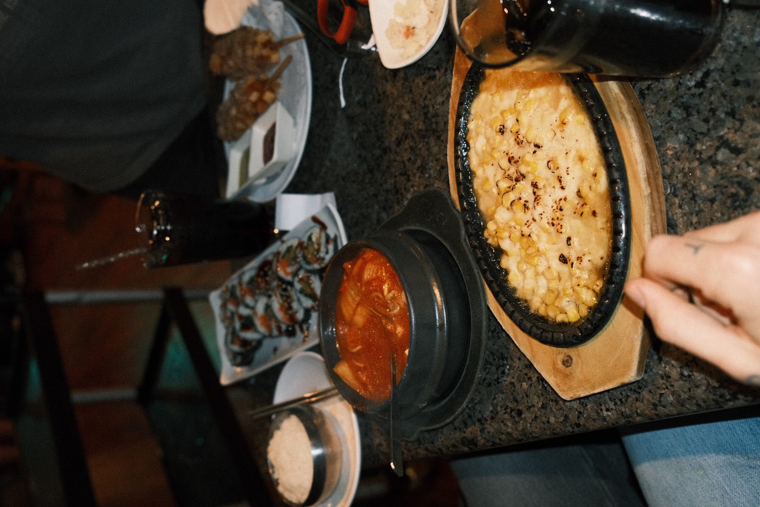 A hand reaches toward a casserole dish of baked rice on a kitchen counter beside bowls of food.