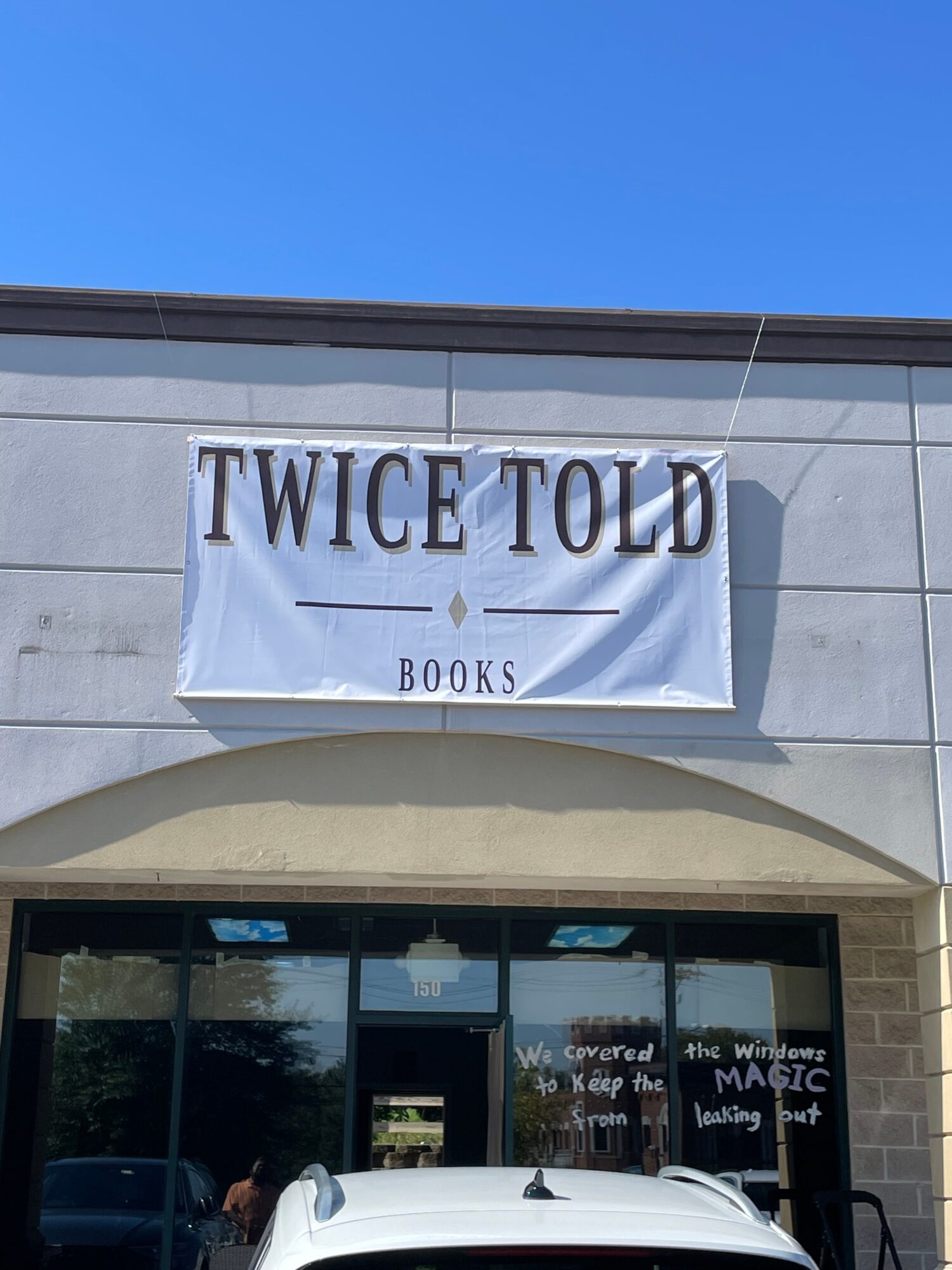 A bookstore storefront with a sign reading “Twice Told Books” above the entrance and a white car parked nearby.