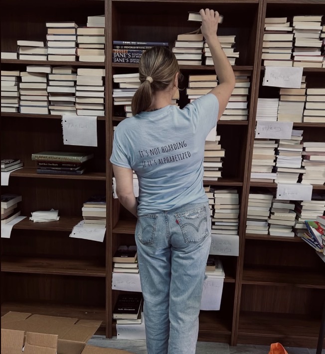 Person reaching for a book on a shelf filled with books and papers.