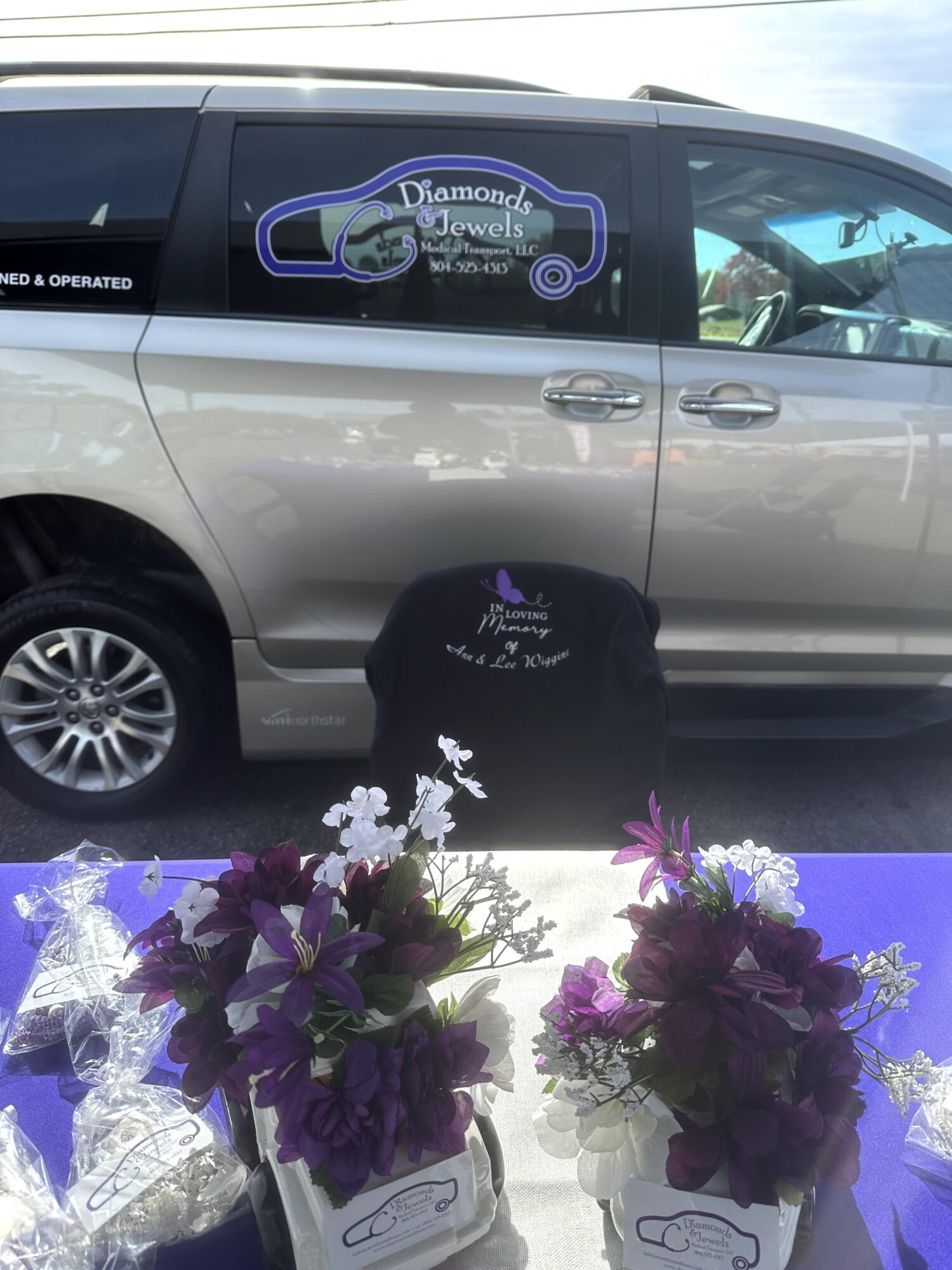 Silver minivan with a jewelry business decal parked behind two floral arrangements.
