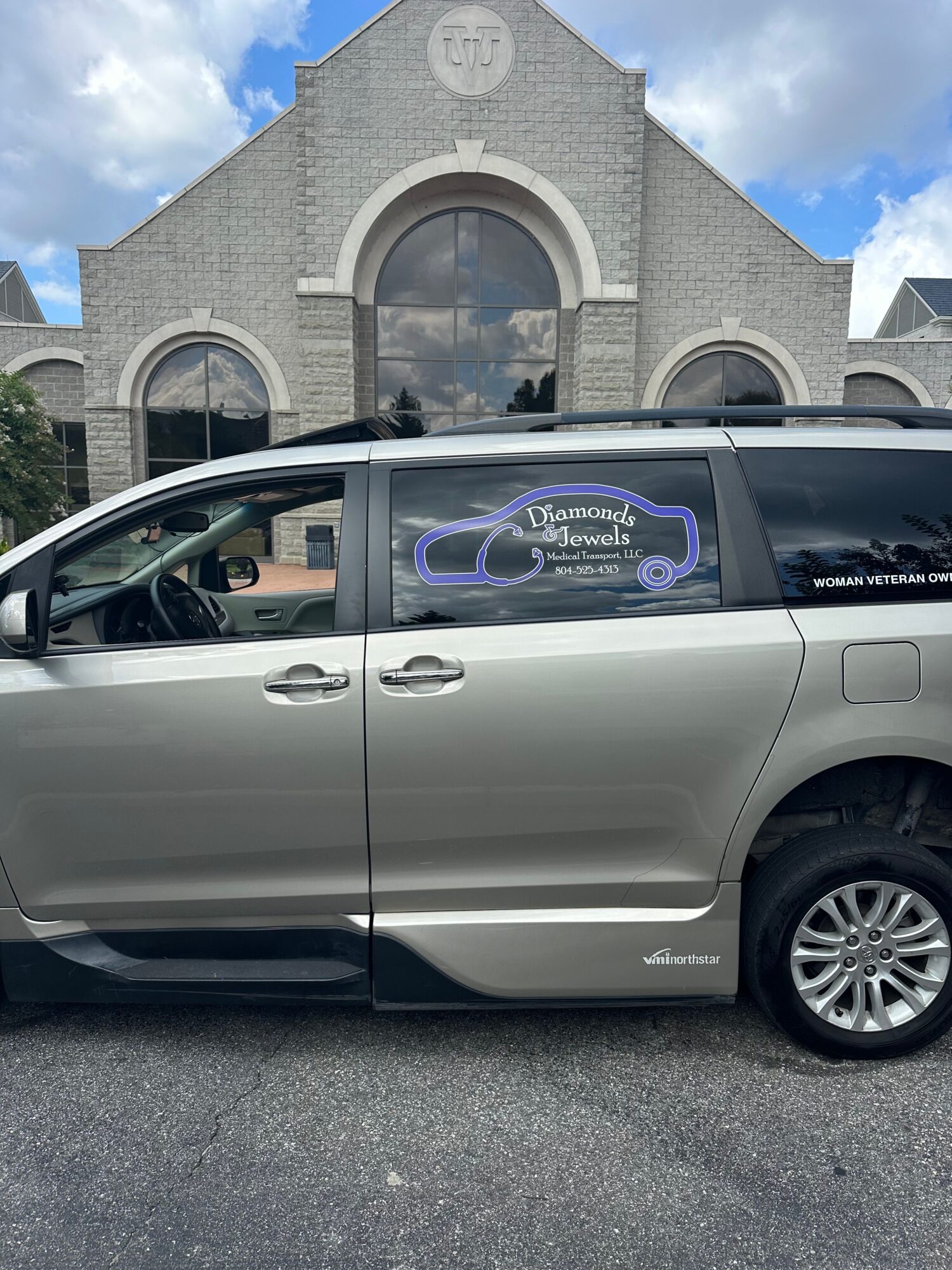 Silver minivan parked in front of a stone building with arched windows.