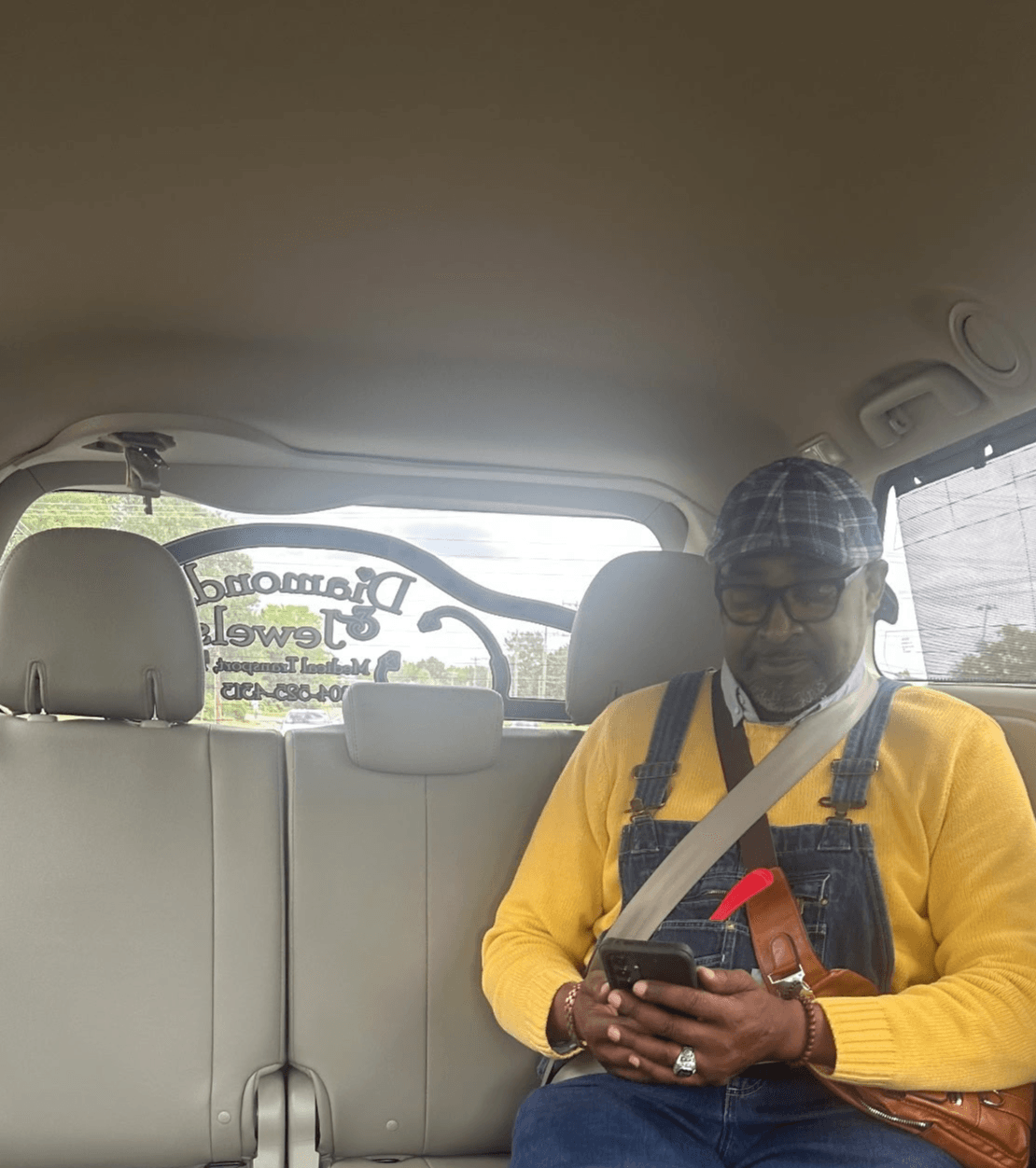 Person wearing a yellow sweater and seat belt looks at a phone inside a vehicle.