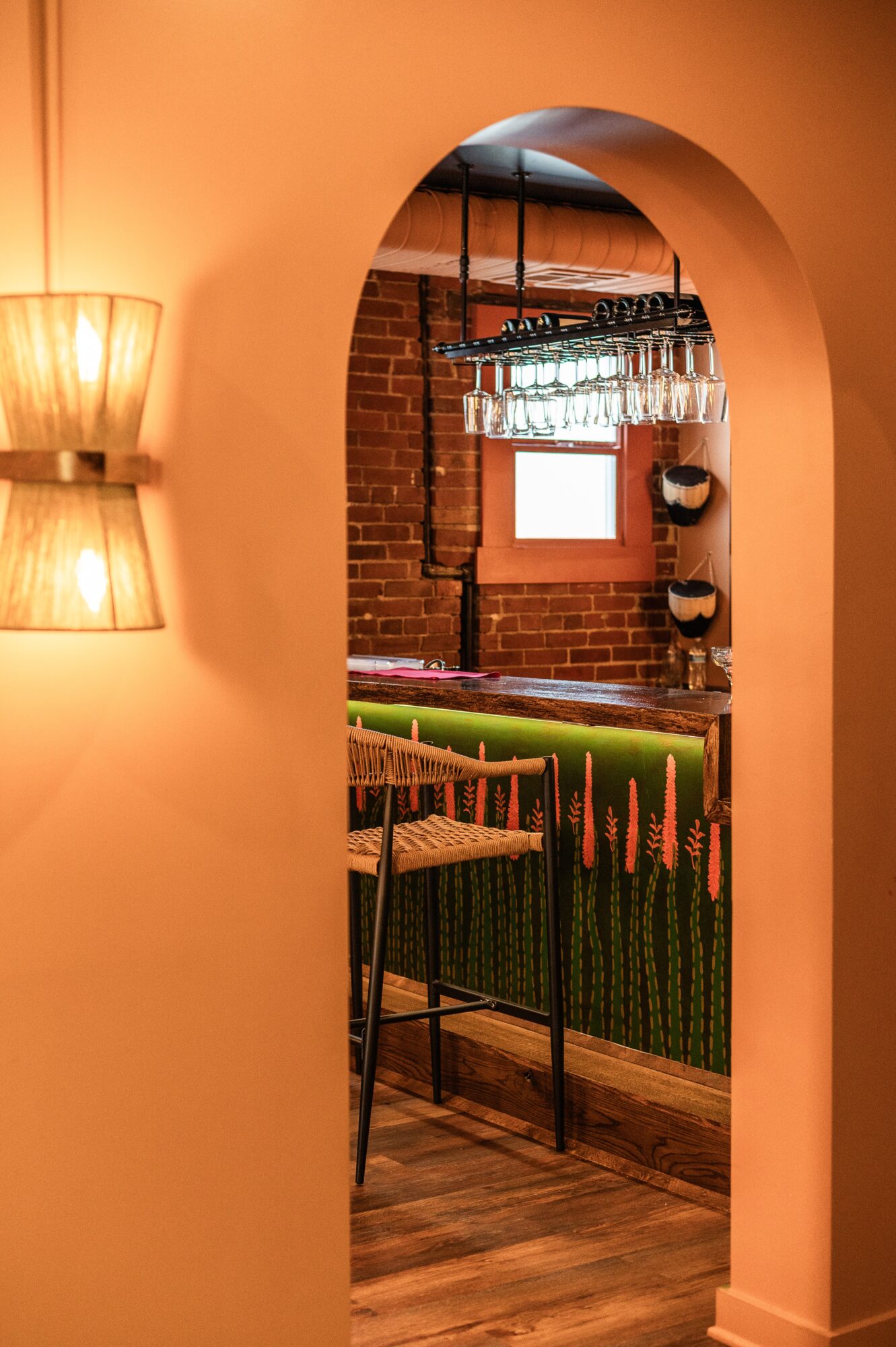 Arched doorway opens onto a bar with hanging glasses, stools, brick walls, and warm wall lighting.