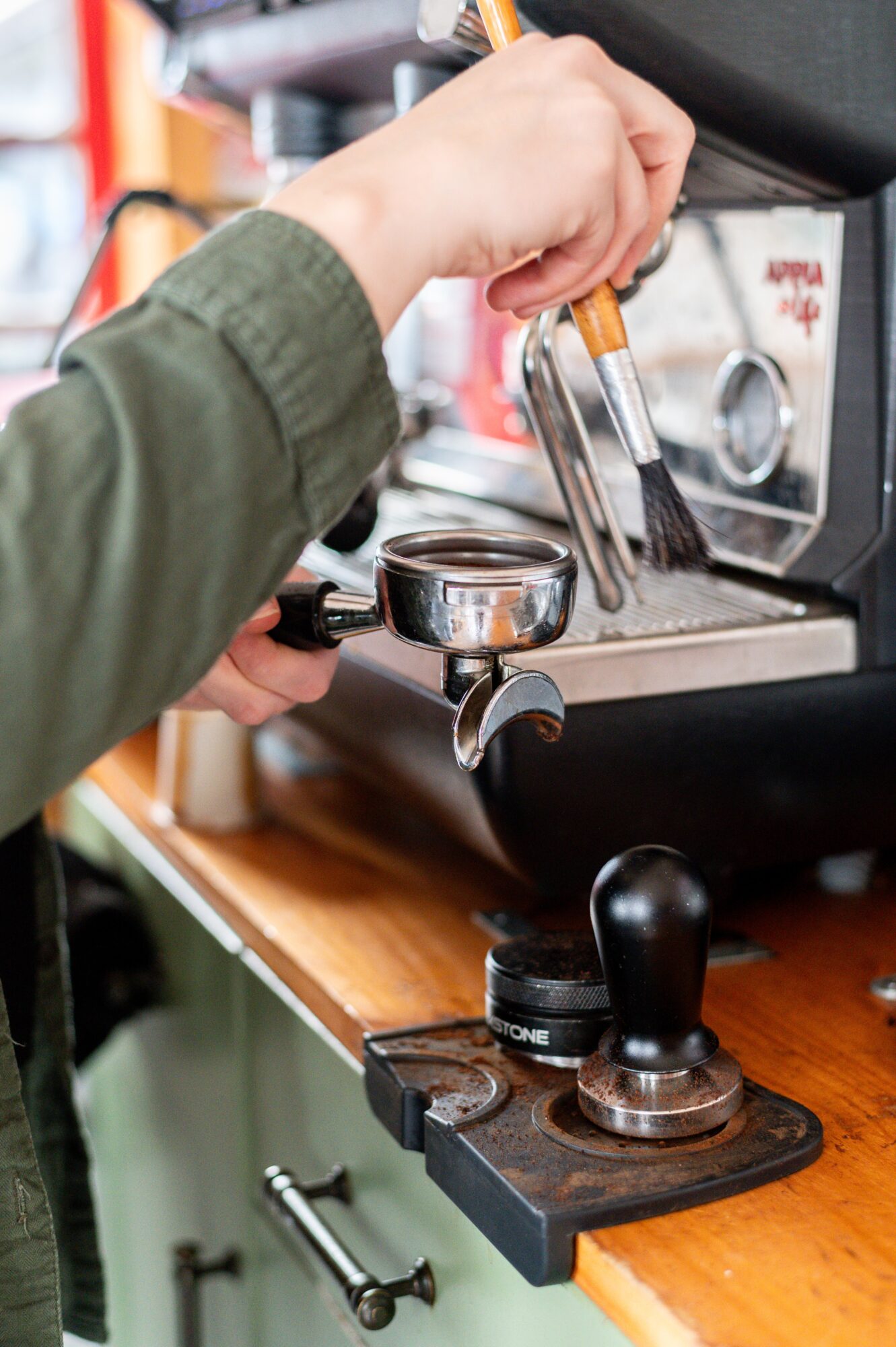 A person operates a commercial espresso machine, holding a metal portafilter near the group head.