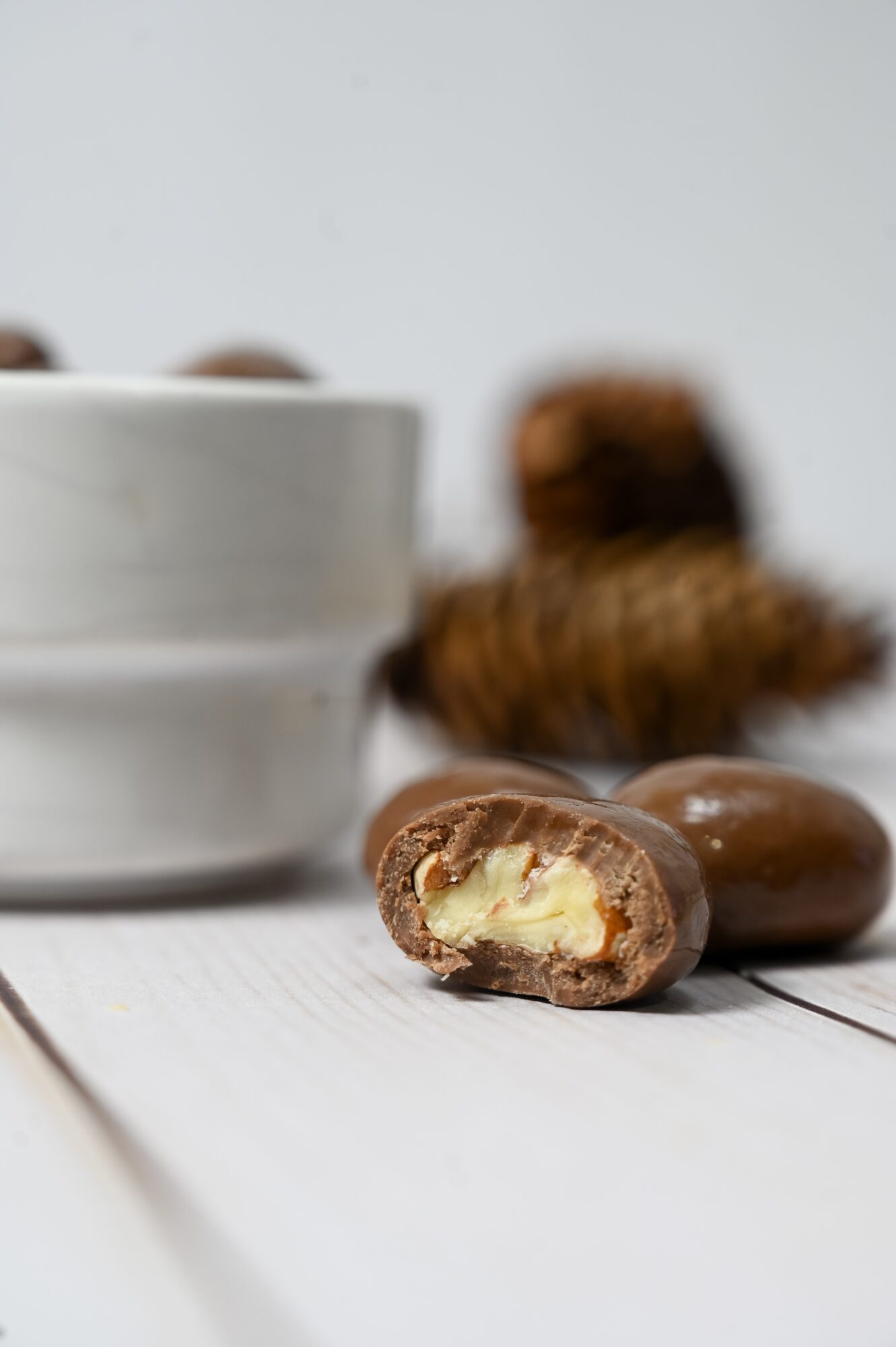 A cut chocolate-covered pastry with pale filling sits on a white surface beside whole pastries and a white cup.