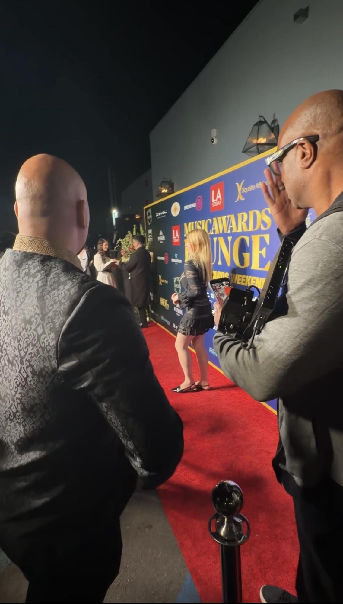People stand along a red carpet in front of a colorful event backdrop.