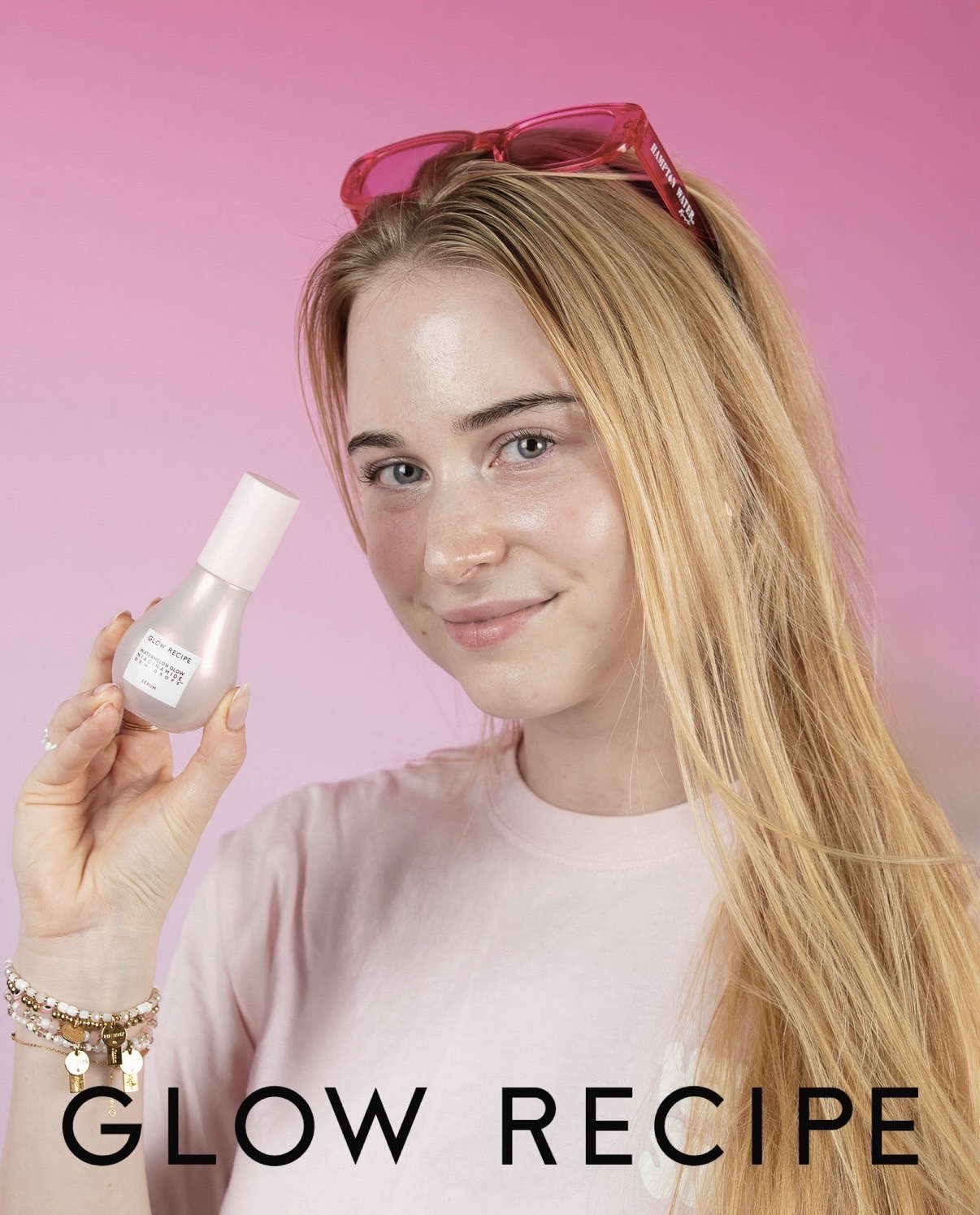 Person with long blonde hair holds a skincare bottle against a pink background; “GLOW RECIPE” appears below.