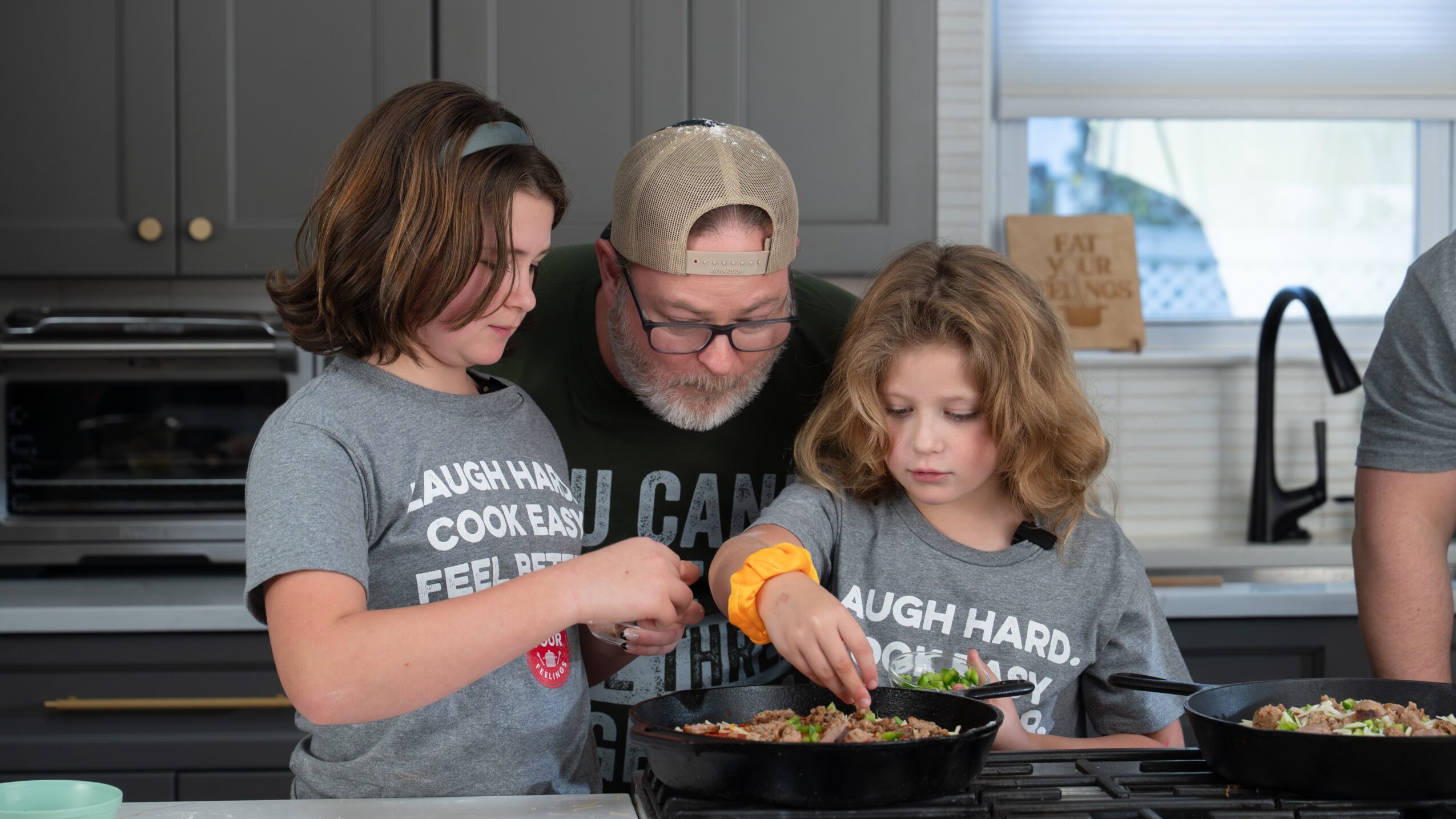 An adult and two children prepare food together at a kitchen counter.
