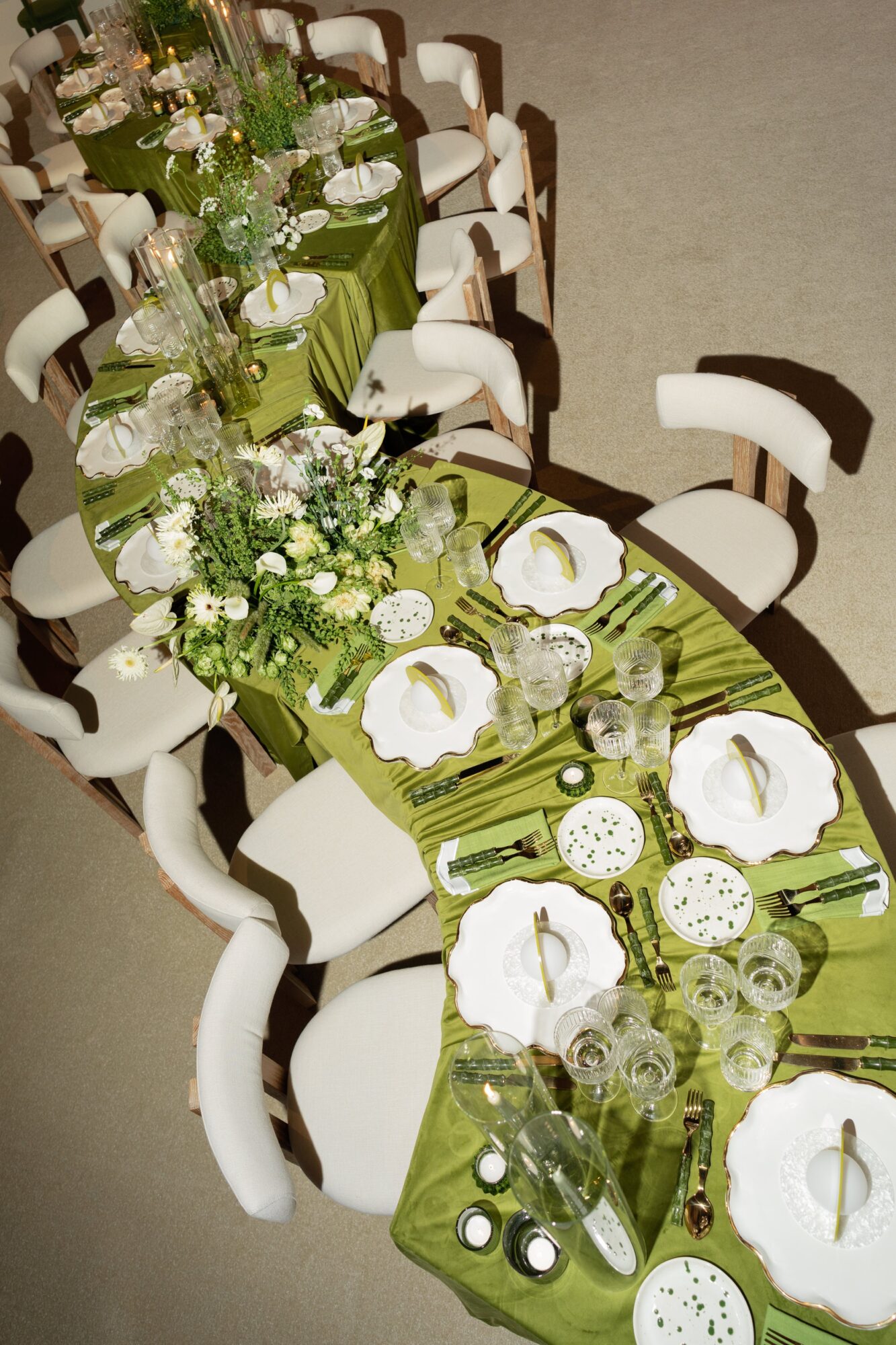 Long dining table set with green linens, white plates, glassware, chairs, and floral arrangements.