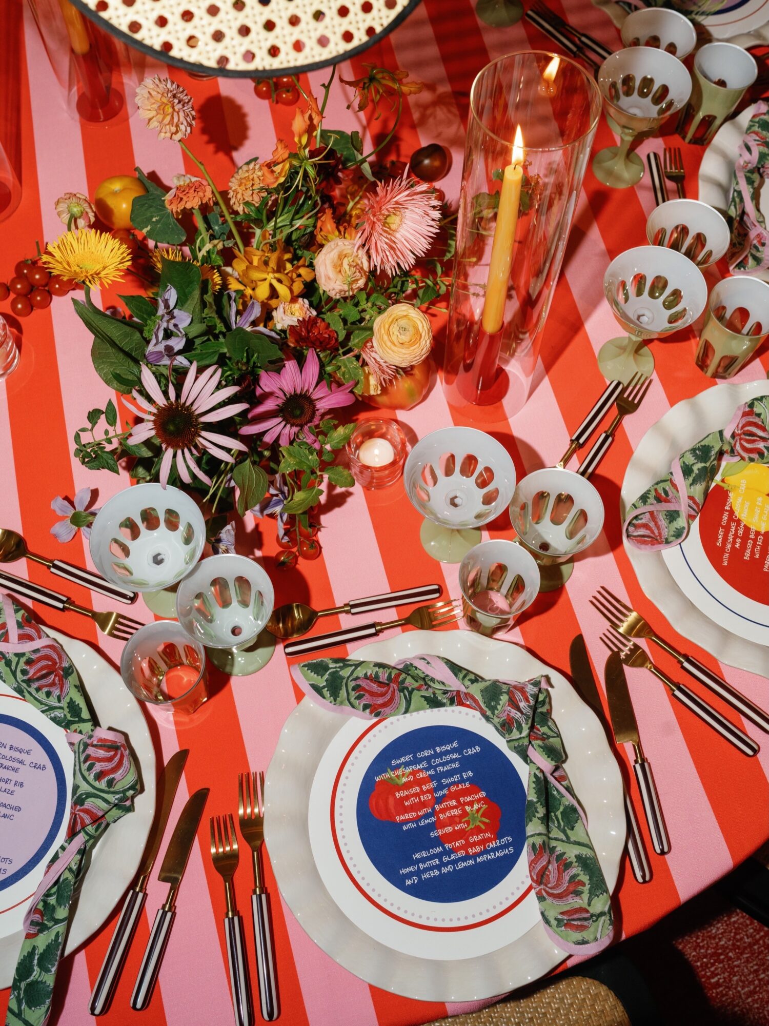 Festive table with flowers, candles, plates, utensils, and a red-and-white striped tablecloth.