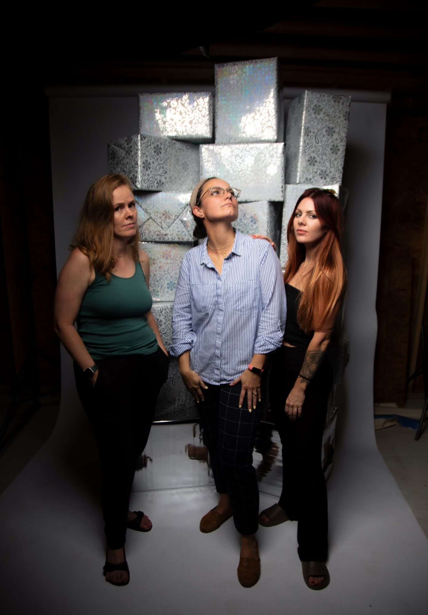 Three people stand beneath a wall of reflective square panels in a dim room.