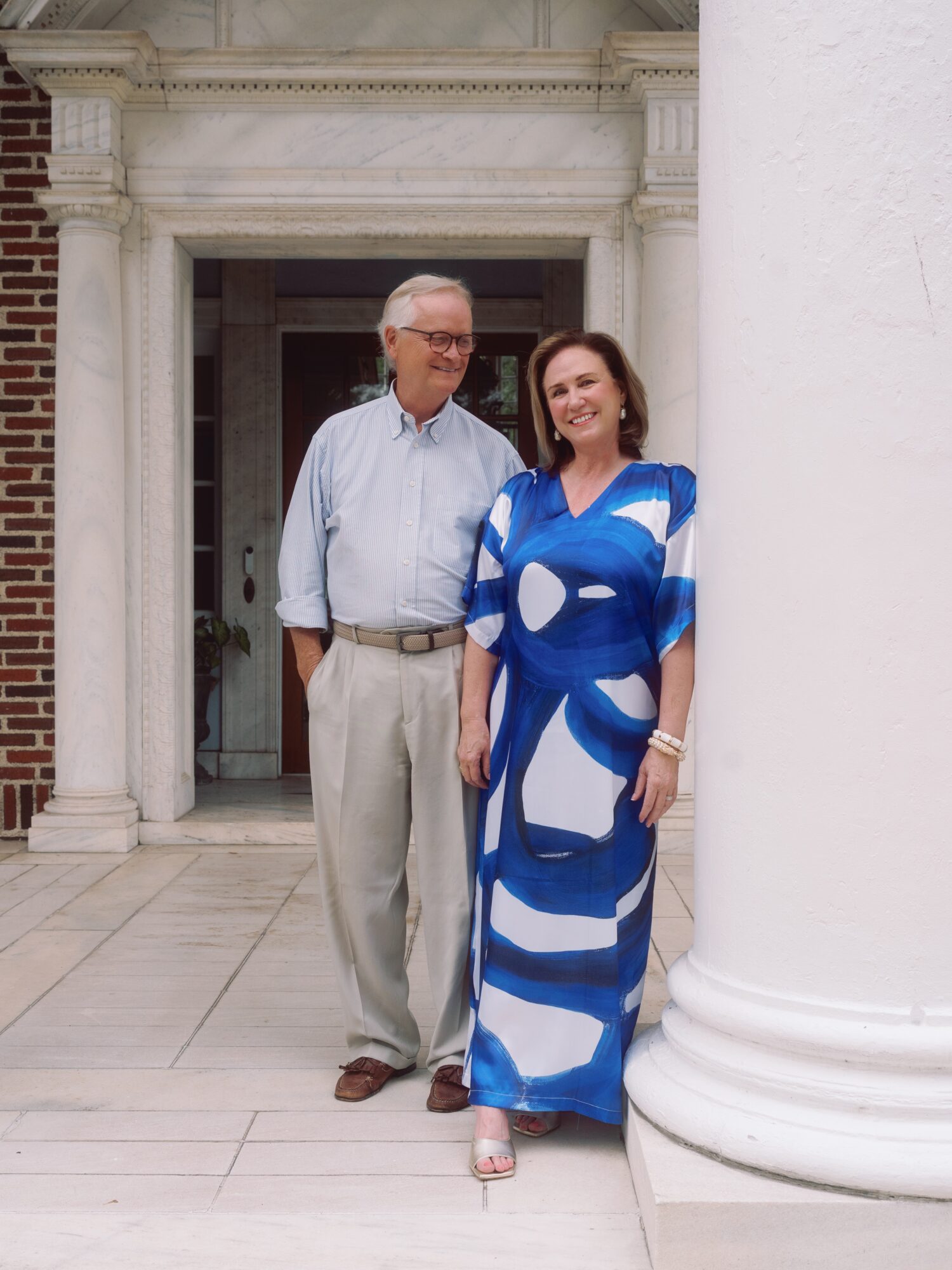 An older man and a woman stand together in a columned doorway.