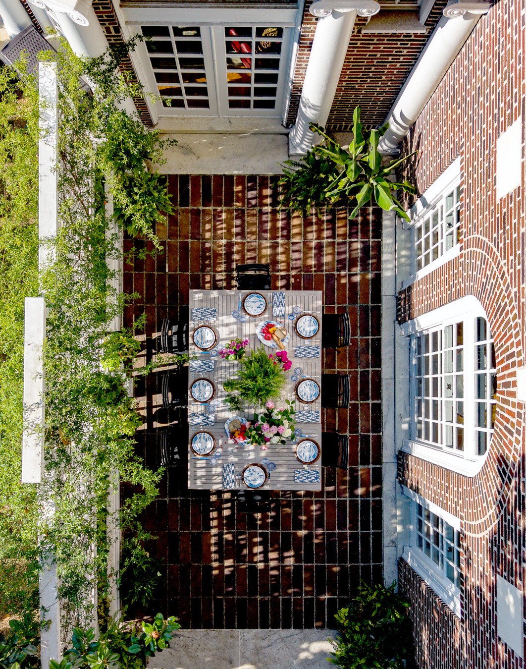 Brick courtyard with a central table, potted plants, windows, and a paved walkway.