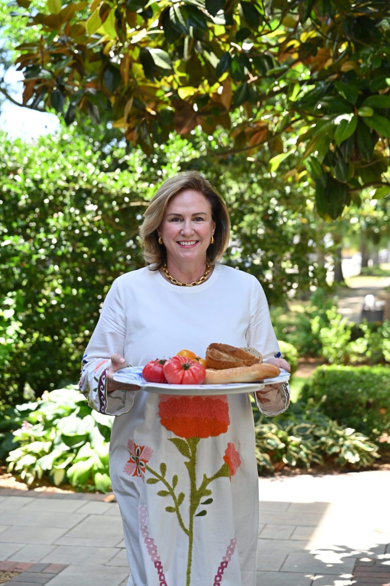 A person holding a plate of food outdoors beside a garden.