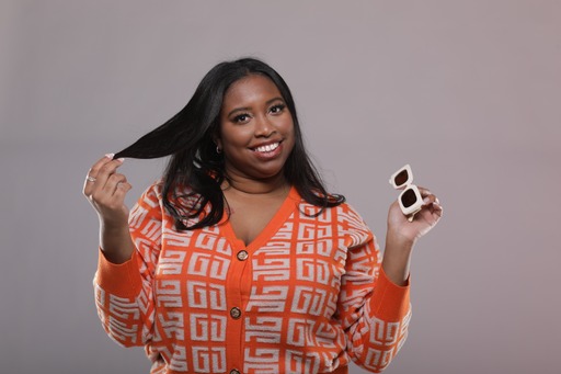 A person in an orange patterned outfit holds a section of their hair and a small compact.