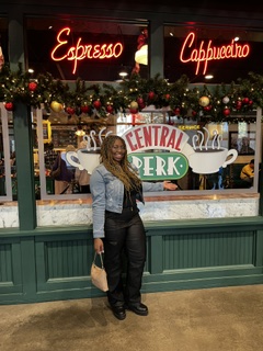 Person standing outside a café with illuminated Espresso and Caffè signs and festive garlands.