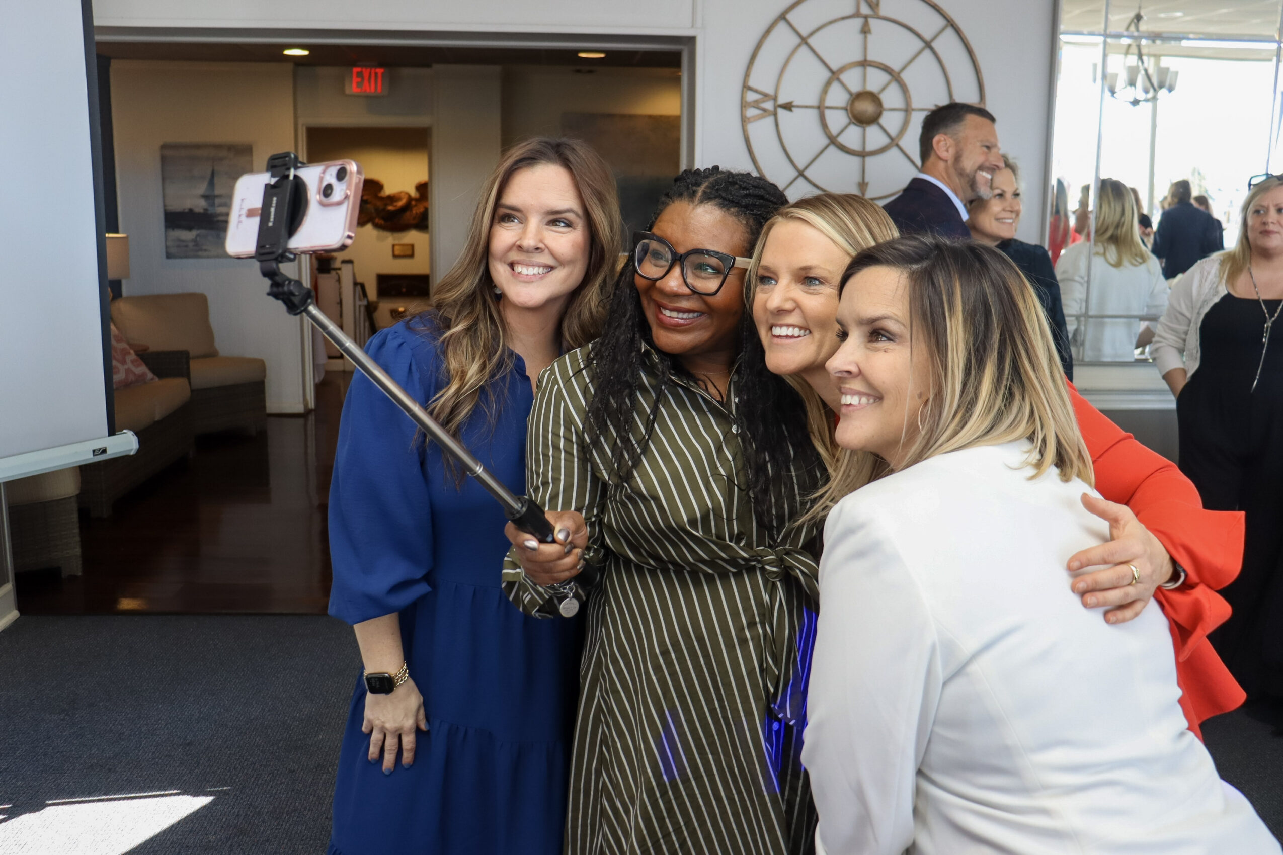Four people pose together for a smartphone selfie in a bright indoor room.