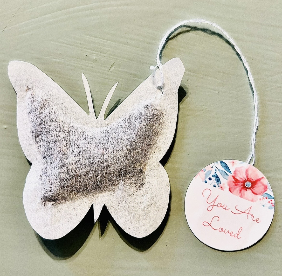 Butterfly-shaped hanging ornament with a round tag reading “You are Loved.”