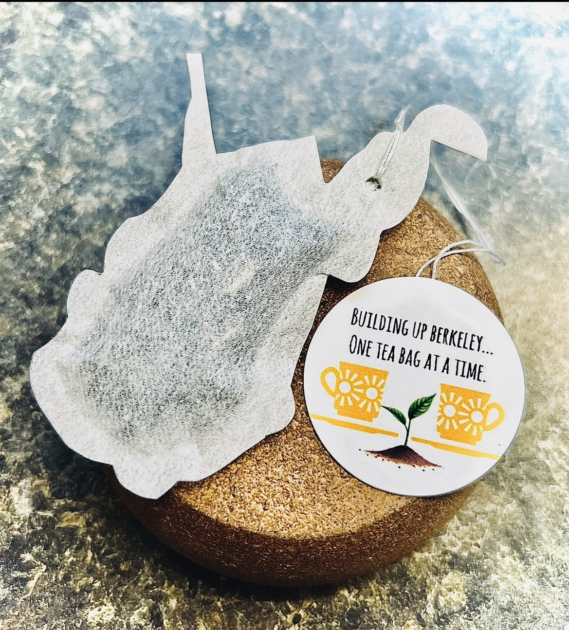 A tea bag with a paper tag rests on a round bed of loose tea leaves.