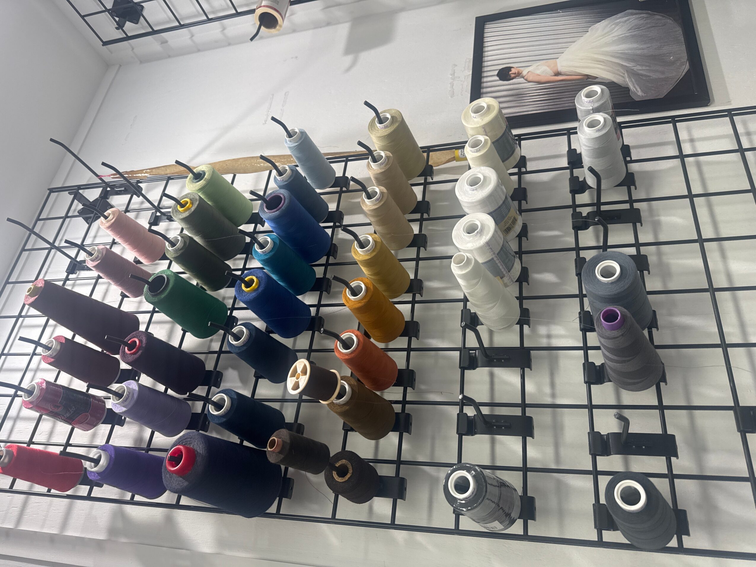 Rows of colorful thread spools on a black grid rack beneath a framed picture.