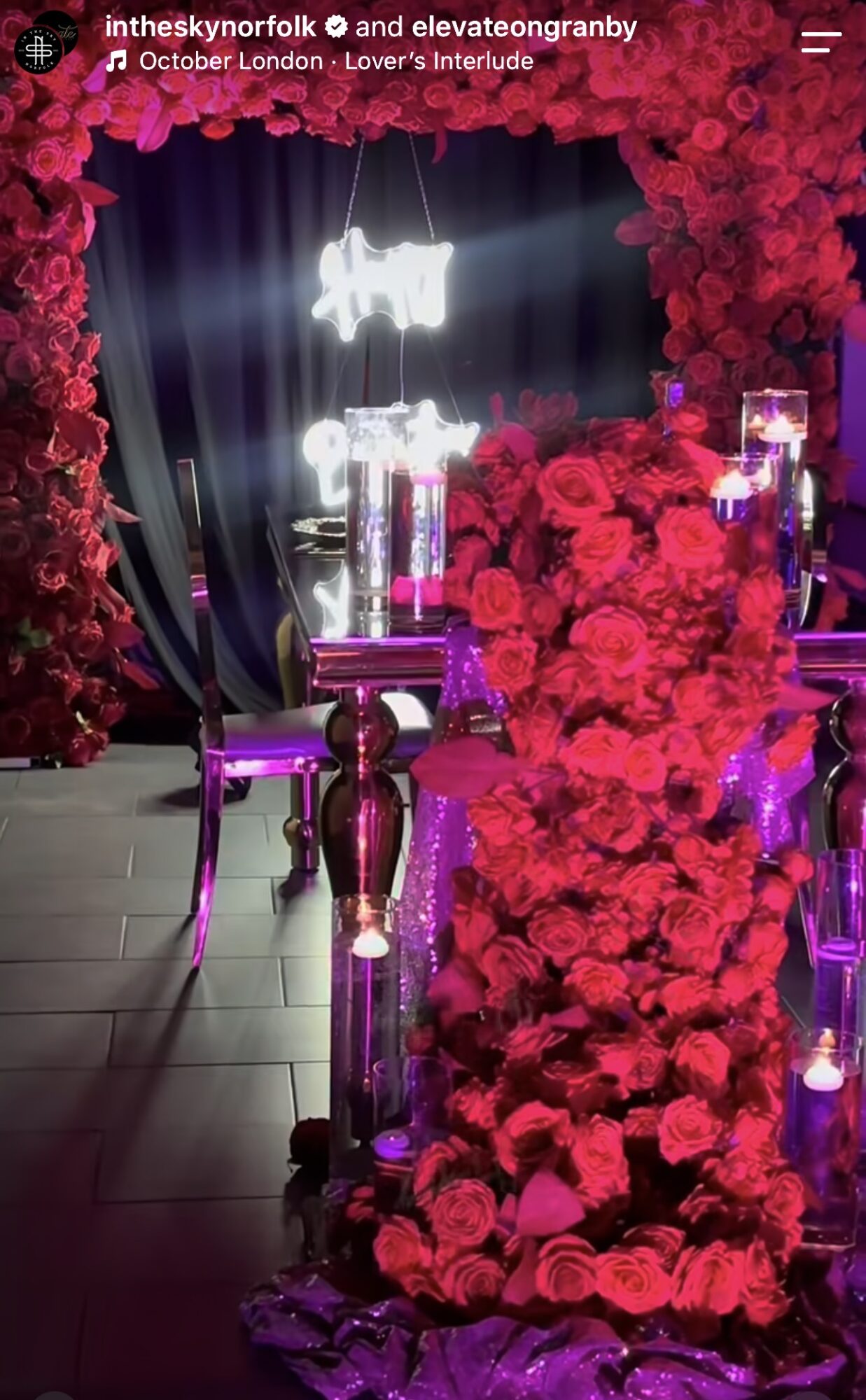 A dramatic display of red roses frames a dark stage with glowing lights and a small table.