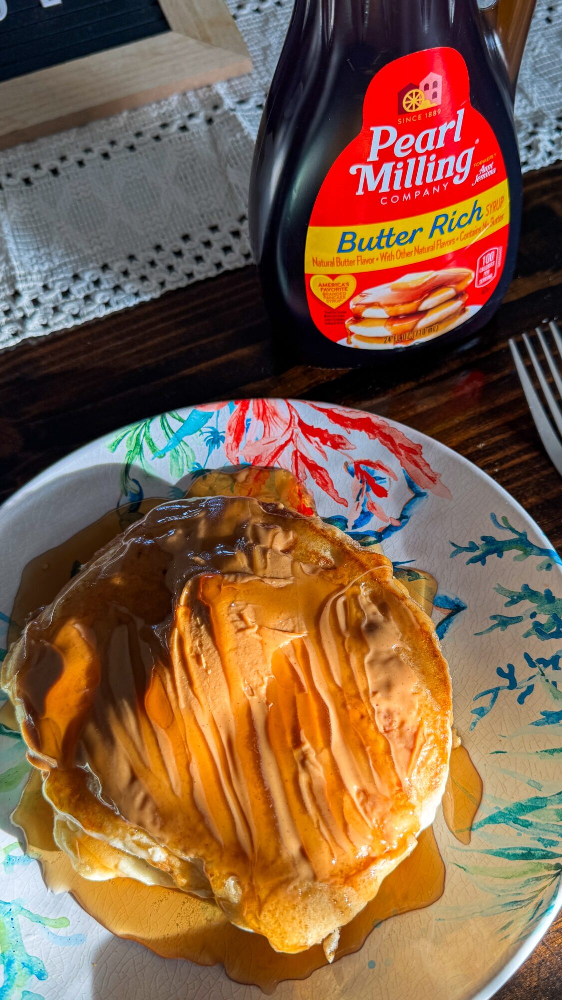 Pancakes topped with syrup on a decorated plate beside a bottle of Pearl Milling Company Butter Rich syrup.