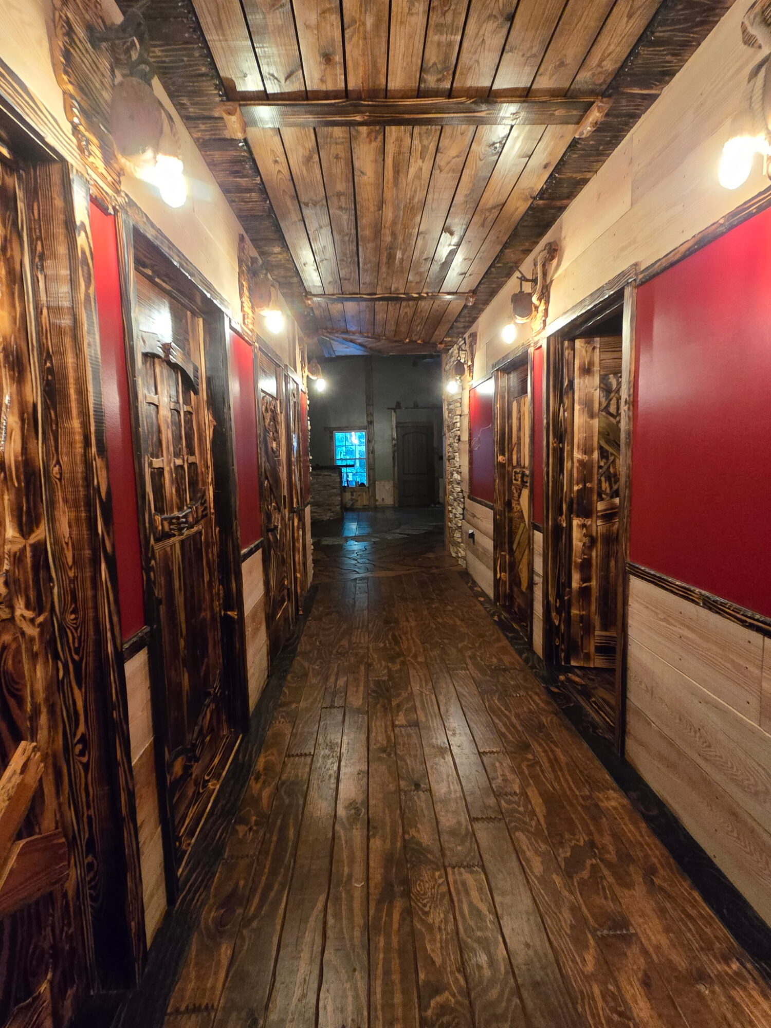 Narrow wood-paneled hallway with doors, wall lights, and a dark wooden floor.