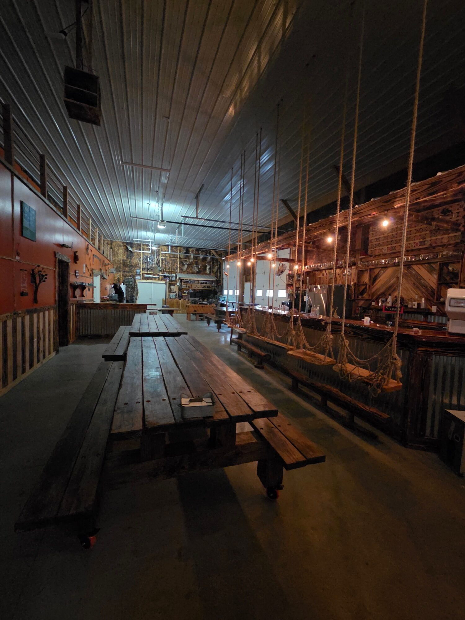 A dim industrial corridor with metal walls, overhead pipes, and a long dark floor.