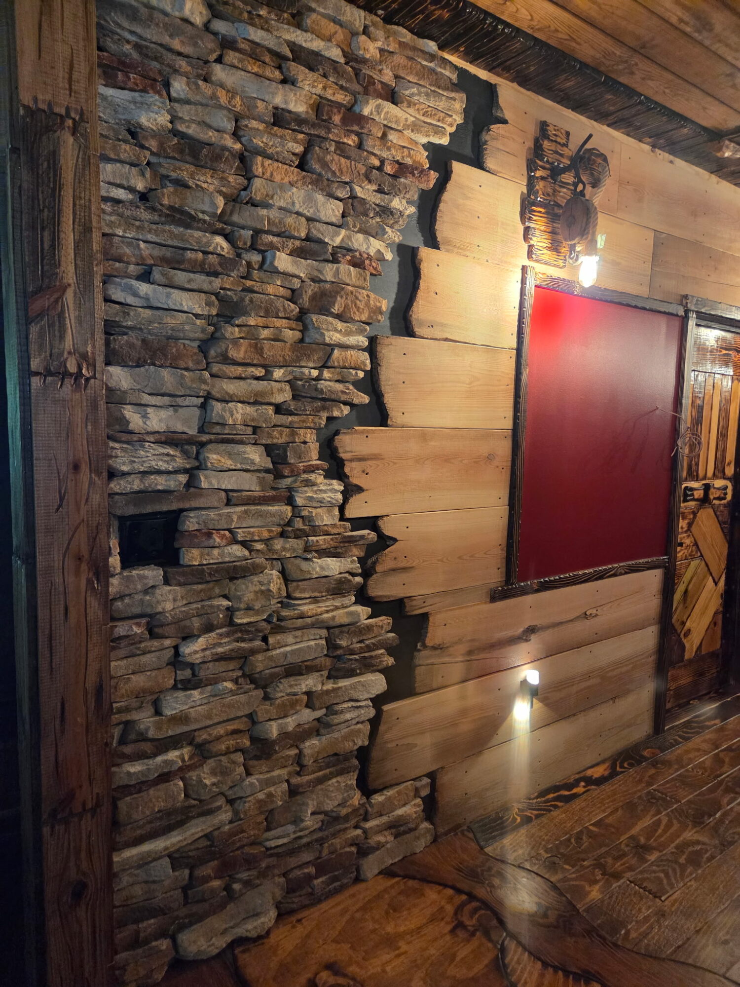 Stone and wood interior wall with a red door, exposed beams, and floor lights.