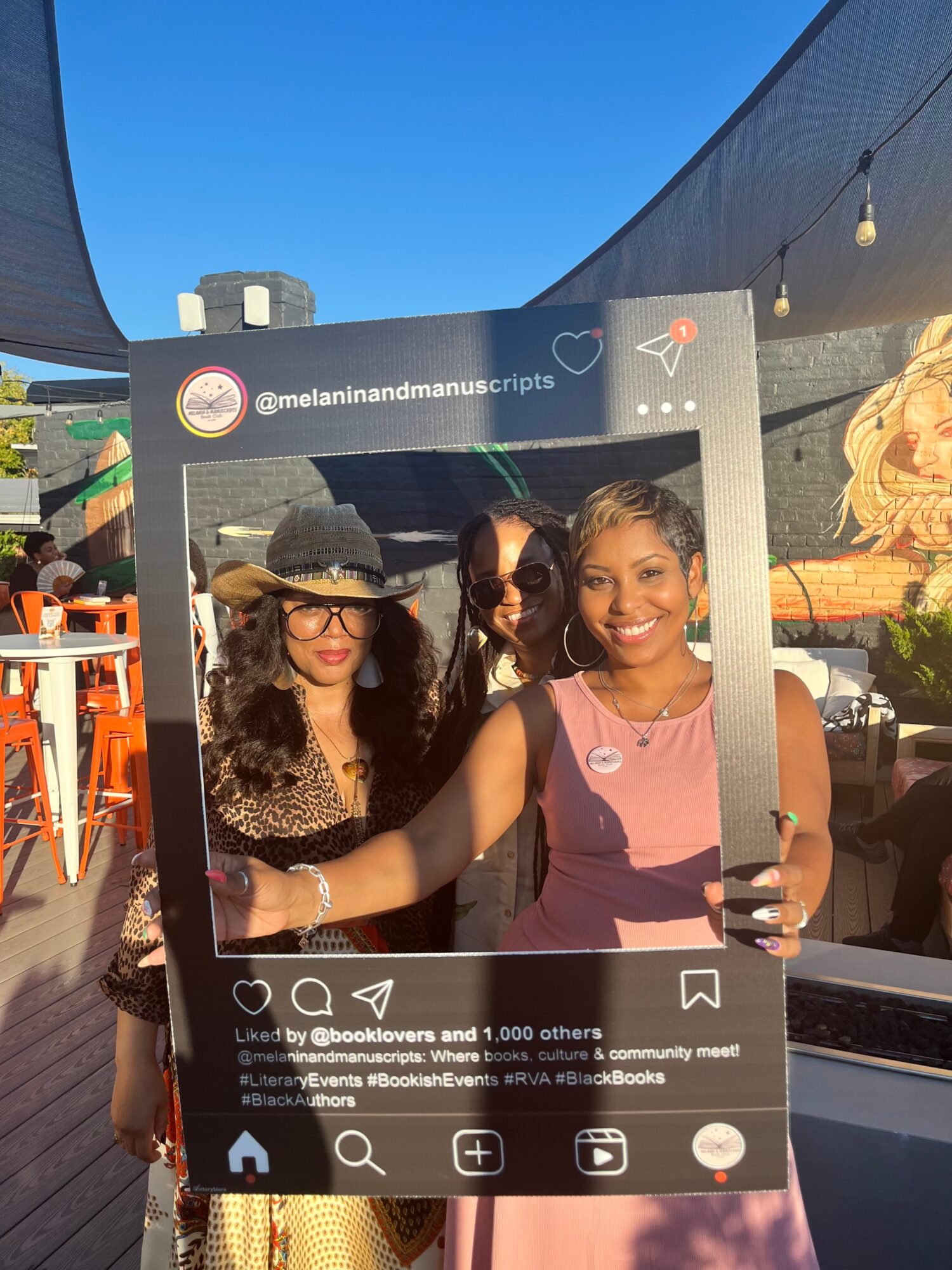 Three people pose behind a large Instagram-style frame at an outdoor event.
