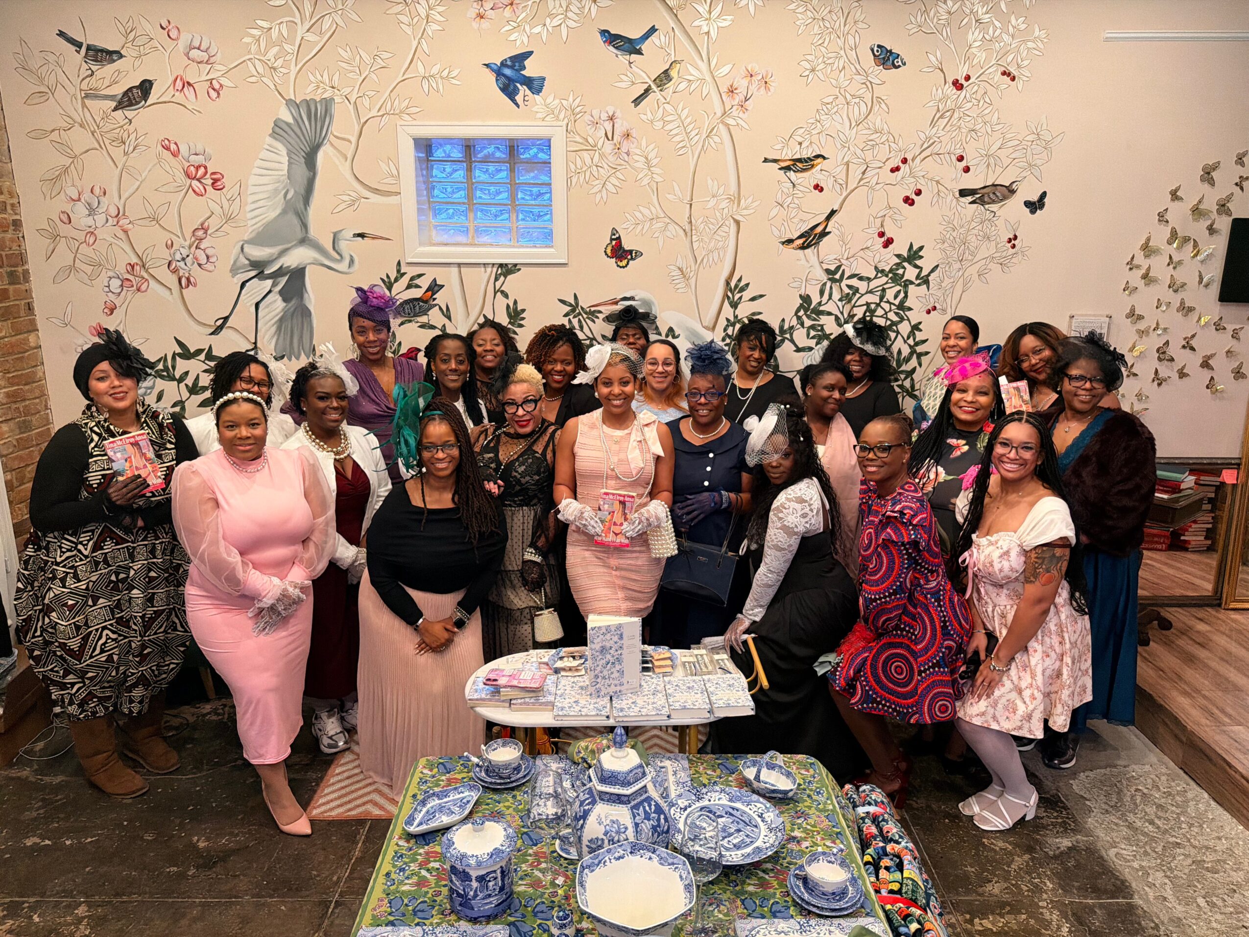 A large group poses behind a table set with blue-and-white dishes in a decorated room.