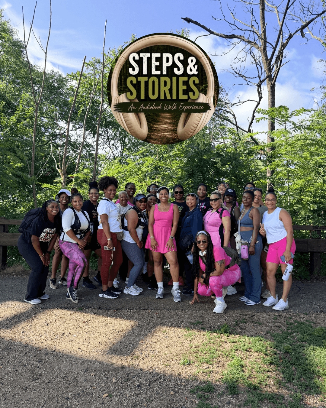 A group of people pose beneath a circular “Steps & Stories” sign in a leafy park.