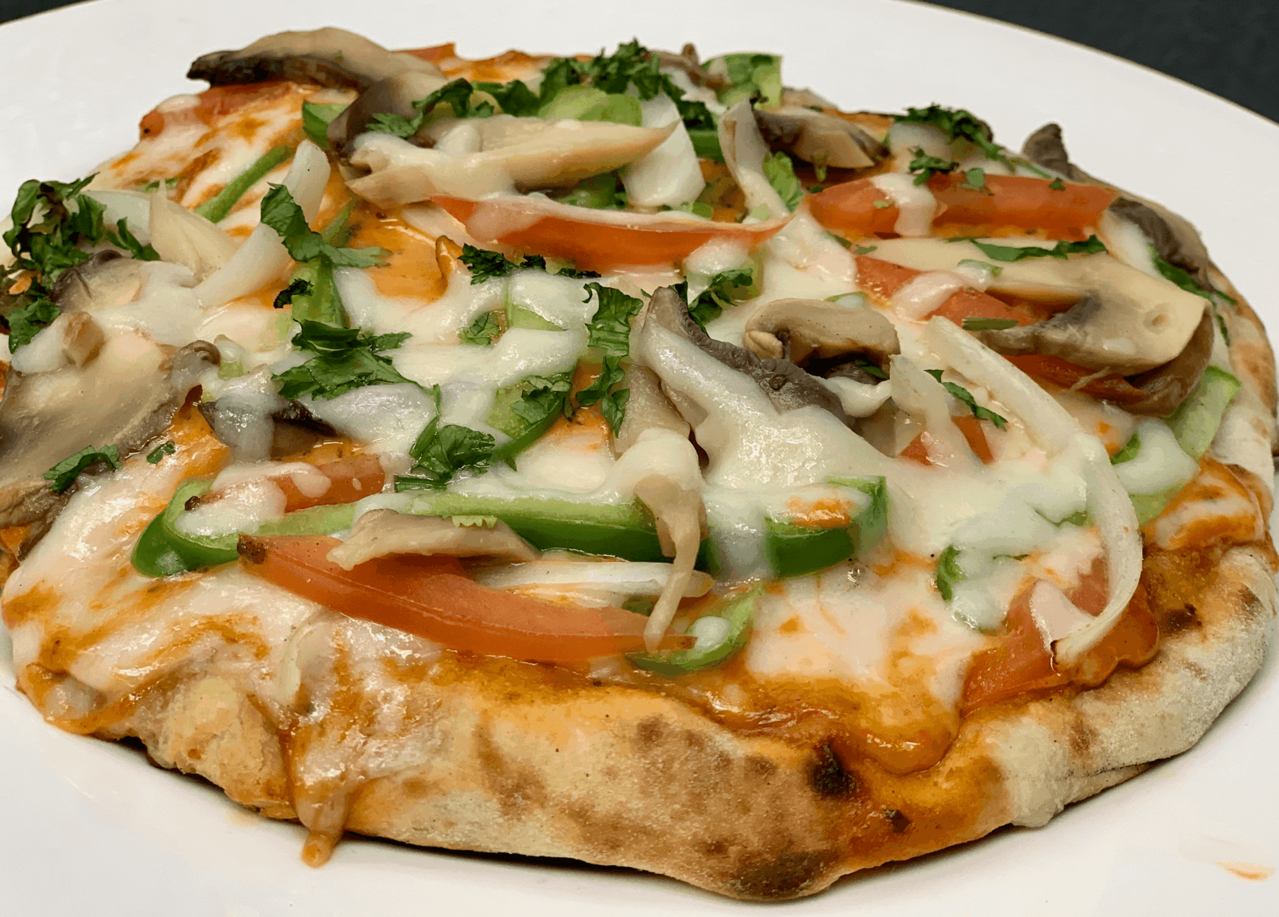 Round pizza topped with melted cheese, tomato, green peppers, mushrooms, and herbs on a white plate.