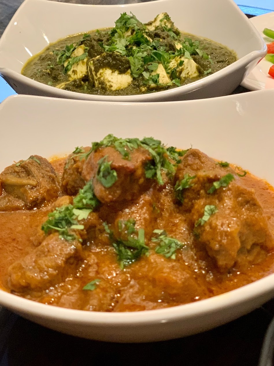 Two white bowls of curry dishes garnished with chopped herbs.